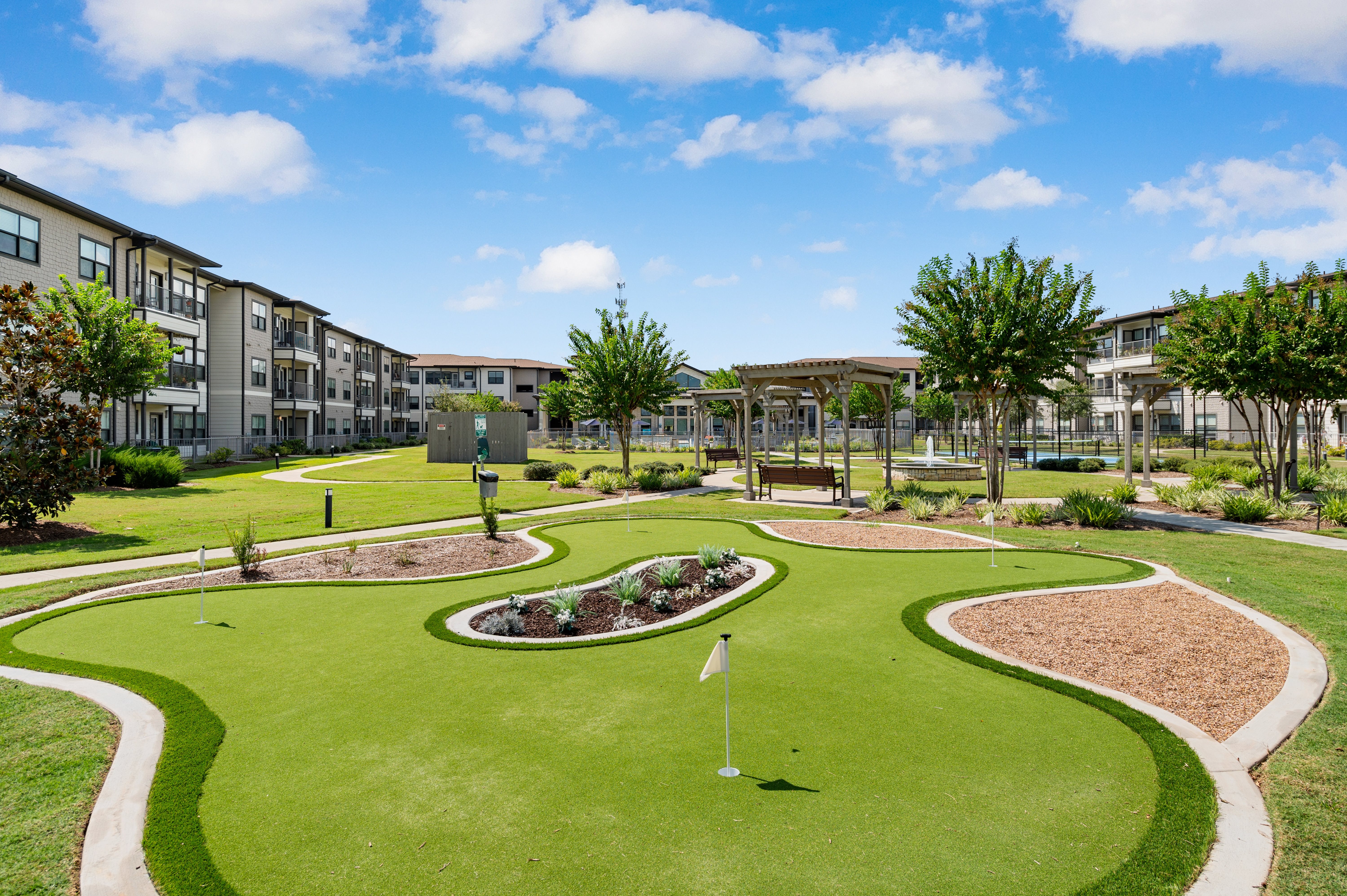 A golf hole is in the middle of a grassy area in front of apartment buildings.