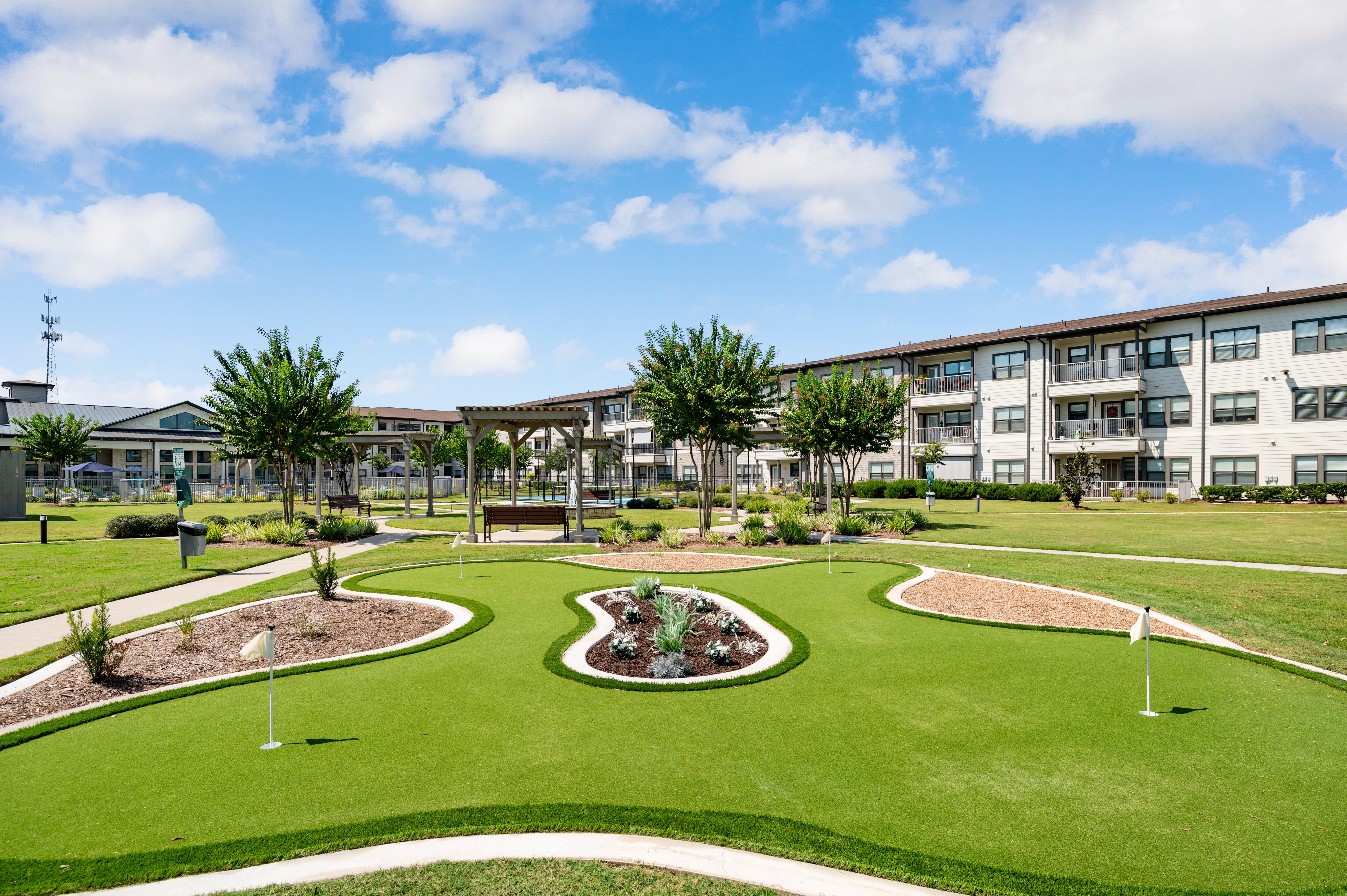 A large grassy area with a circular flowerbed in the middle and apartment buildings in the background.