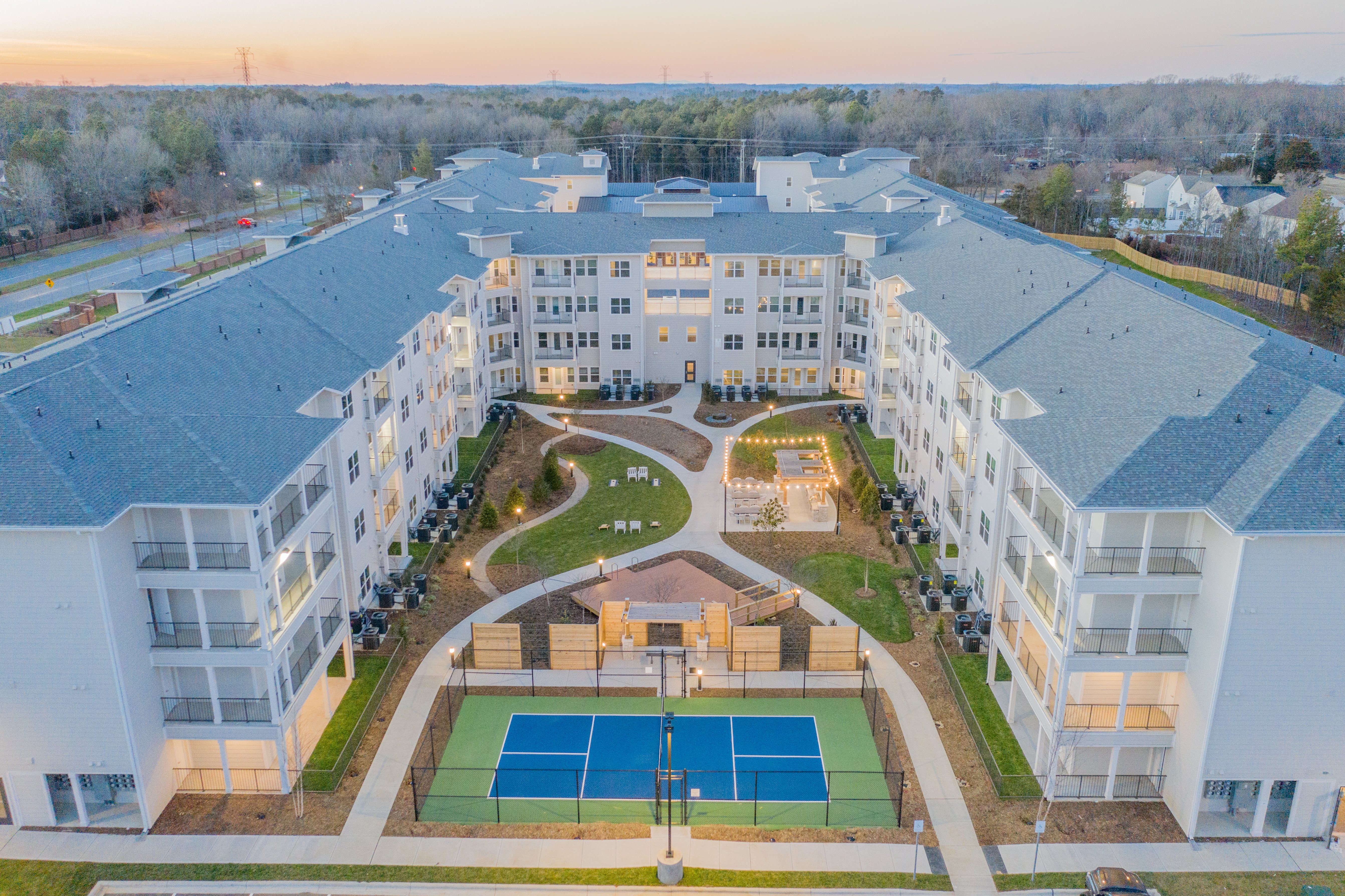A tennis court is located in the courtyard of a large apartment complex.