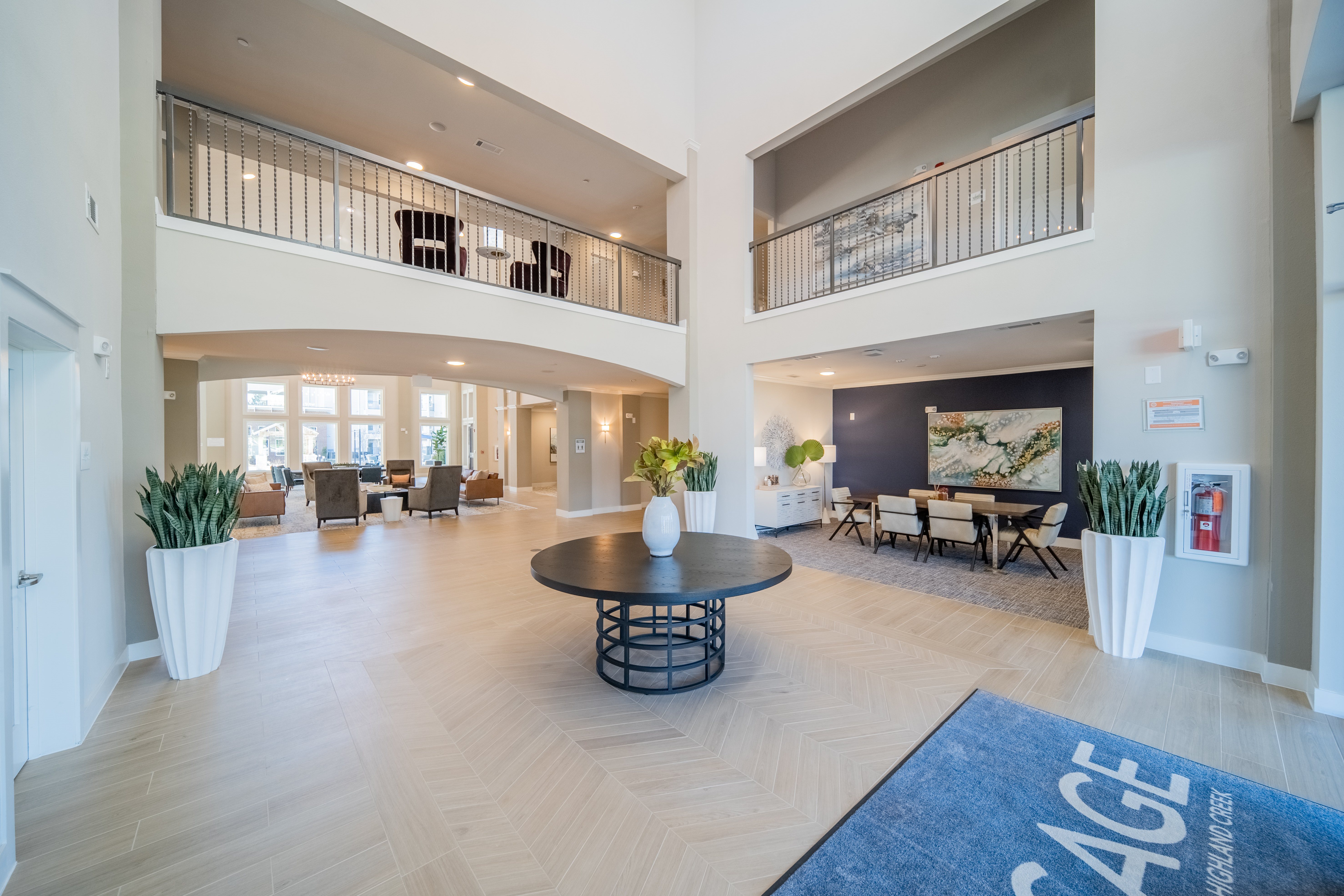 A spacious lobby with a blue rug that reads "AGE" and a large black table in the center.