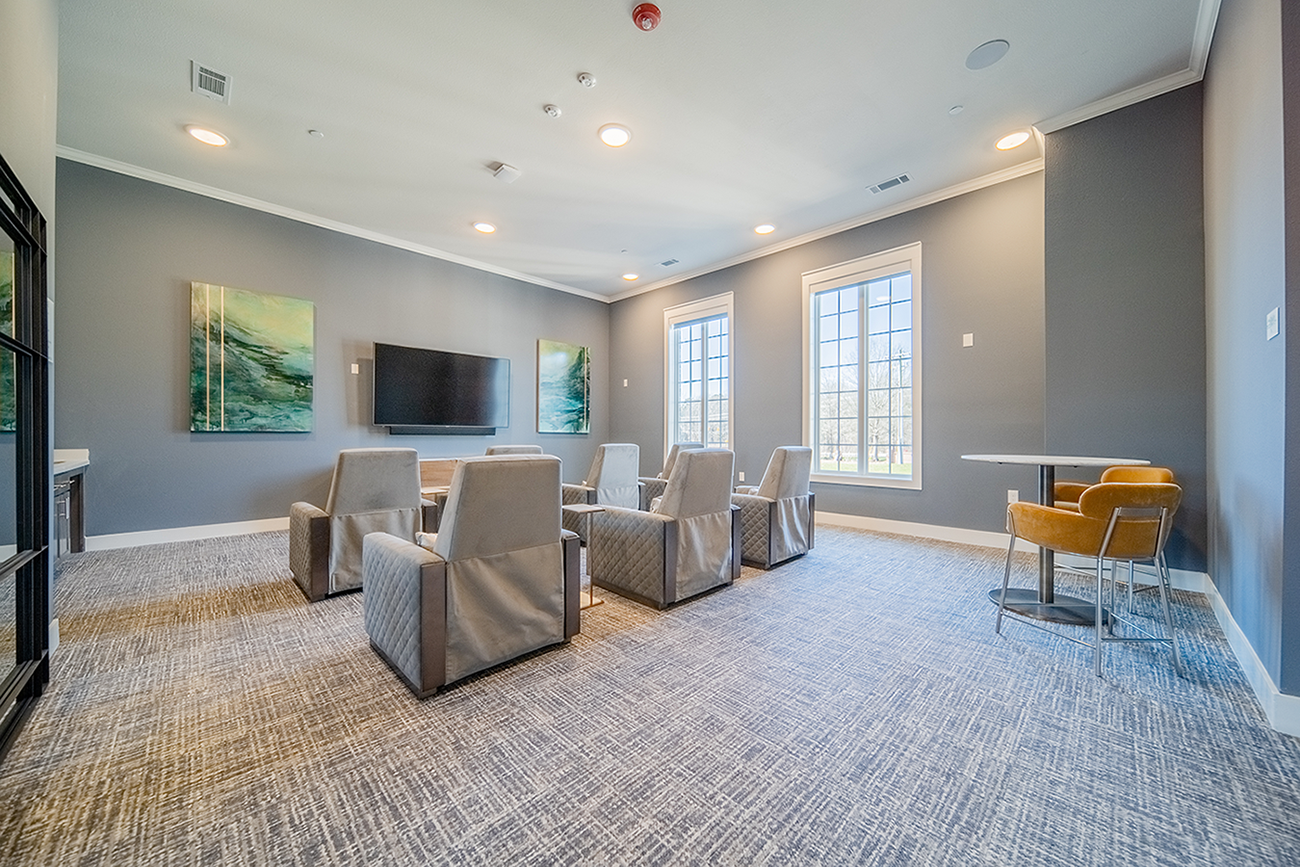 a media room with lounge chairs and a large television at a senior apartment community