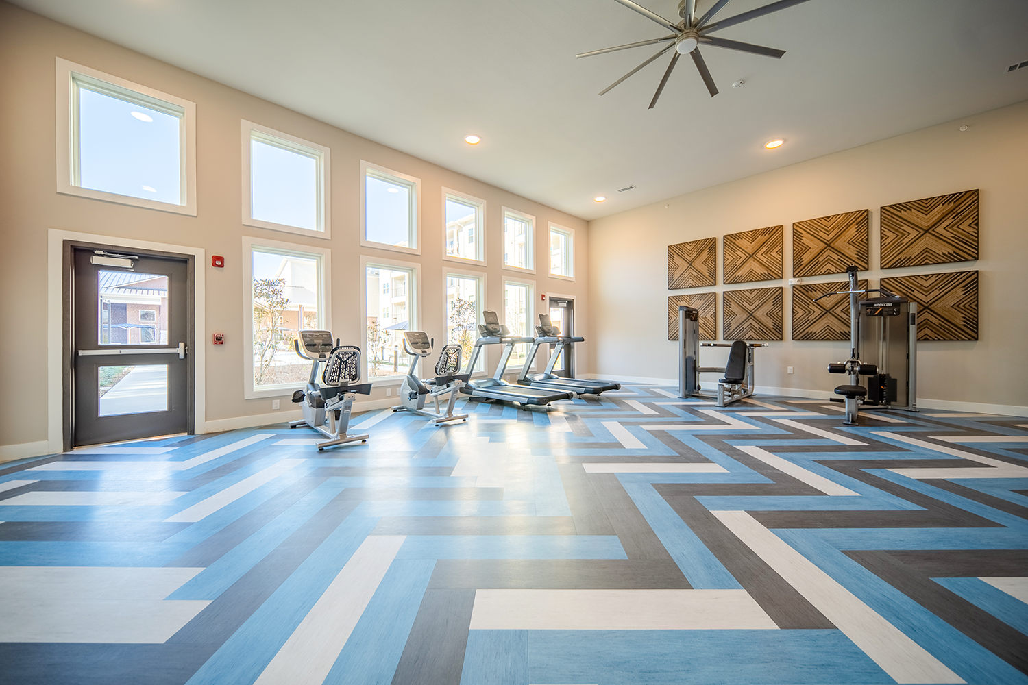 a gym with fitness machines and equipment and a large ceiling fan at a senior apartment community