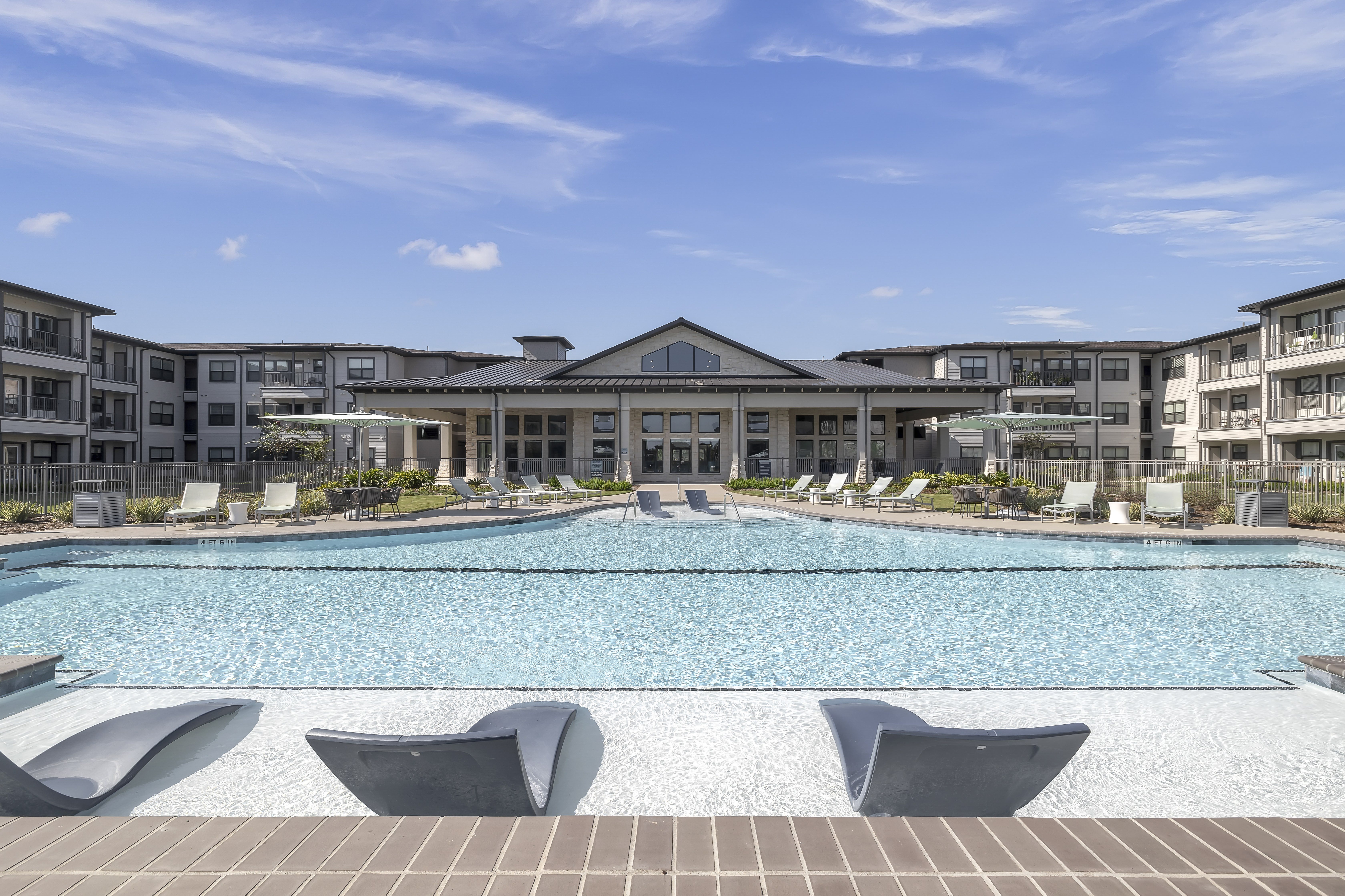 A large swimming pool in front of a building with lounge chairs around it.