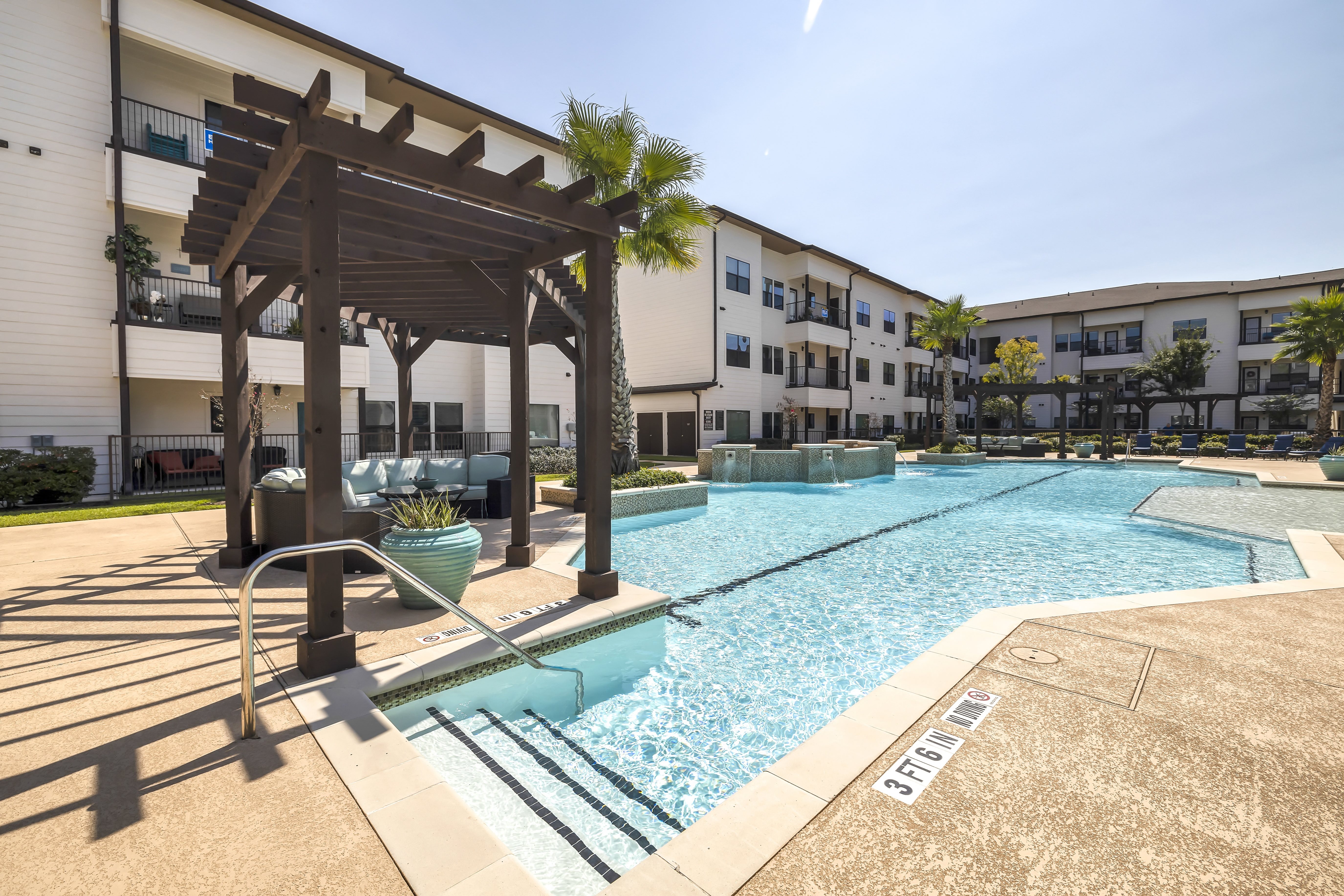 a resort-style pool with a lounge area under a wooden pergola at a senior apartment community