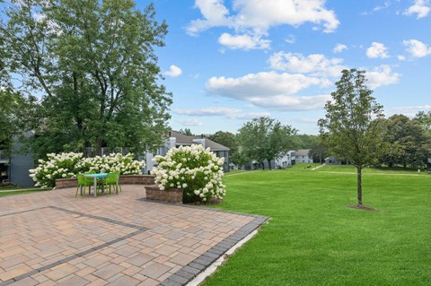 a paver patio with a table and chairs in the middle of a grassy area
