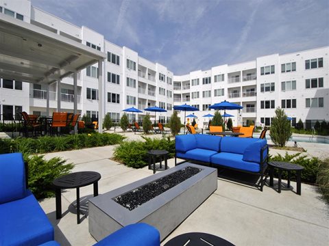 a patio with blue couches and chairs and umbrellas in front of an apartment building at The George, Michigan, 48104