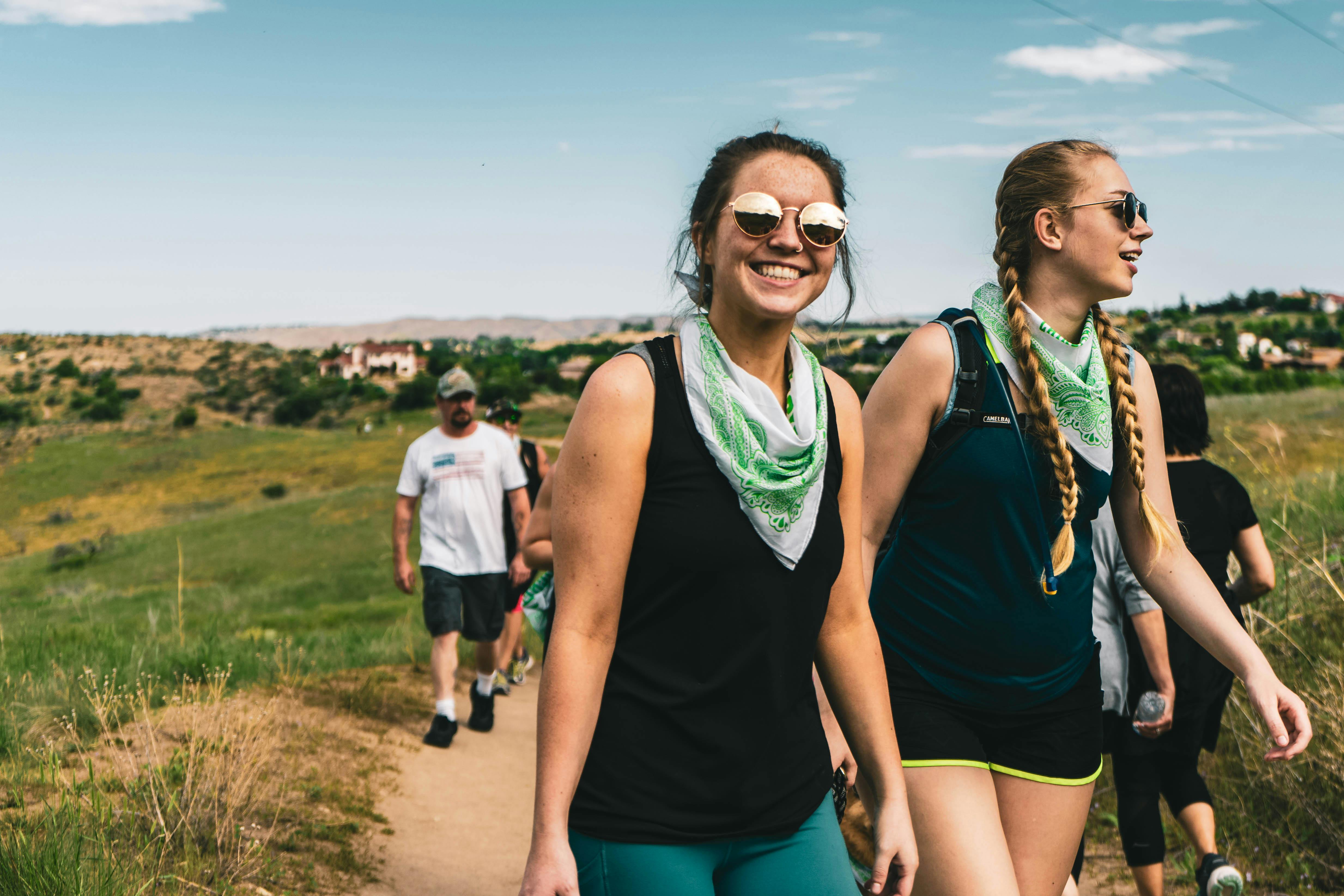 Two women wearing green bandanas smiling while hiking a dirt trail near the Wesley Kensington property.