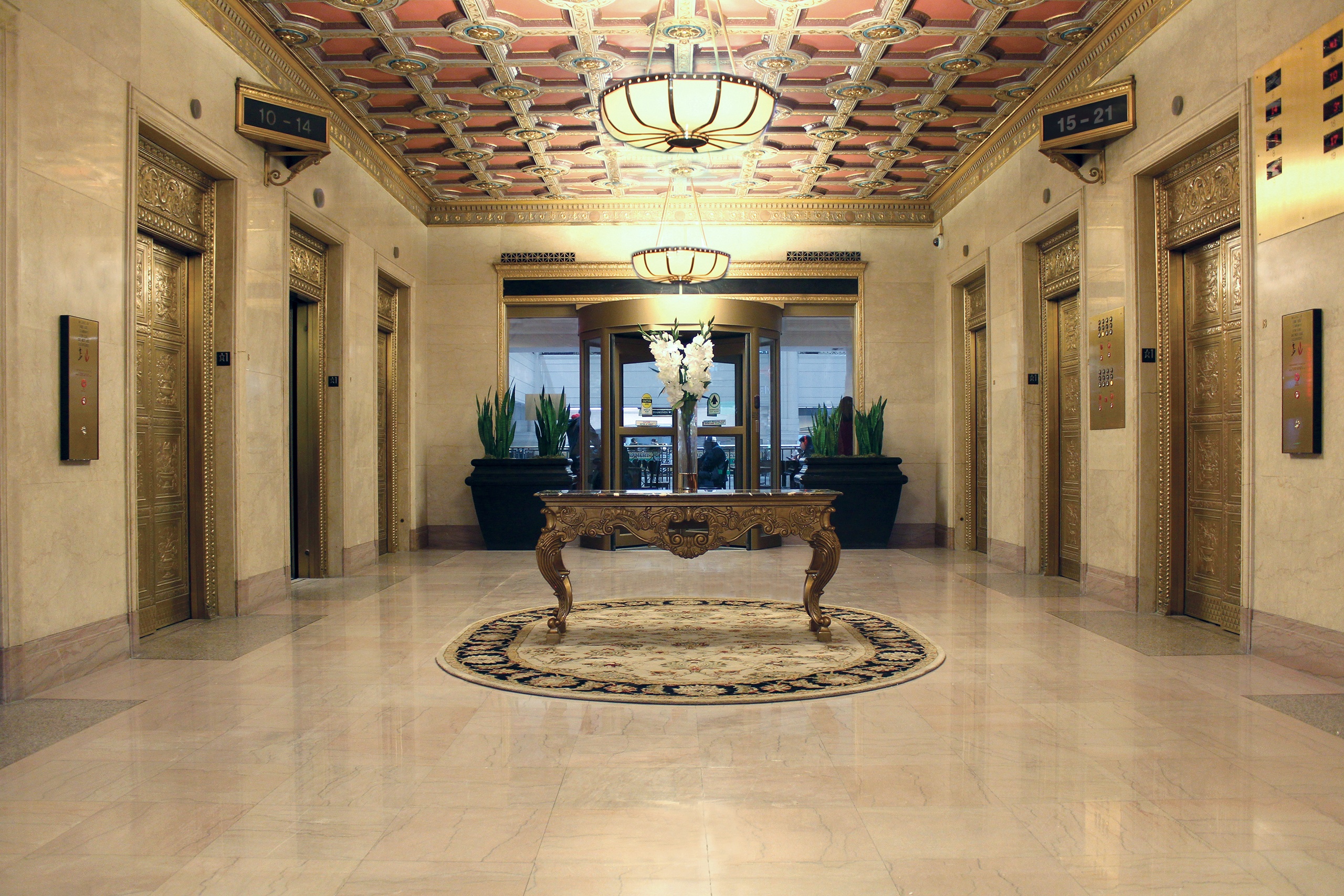 The grand historic lobby of The Terminal Tower Residences in downtown Cleveland, featuring ornate gold-leaf coffered ceilings, marble floors, and elegant brass elevators.