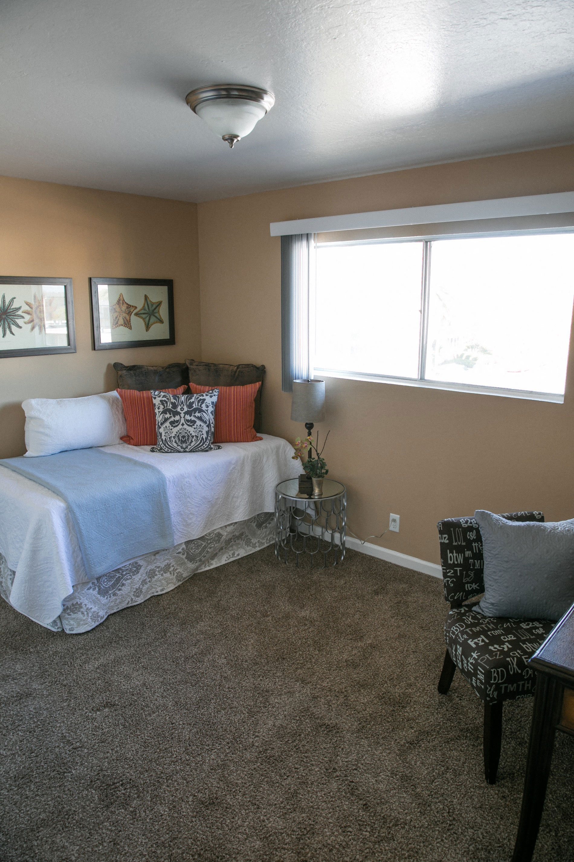 A bedroom with a bed, chair, and two pictures on the wall.
