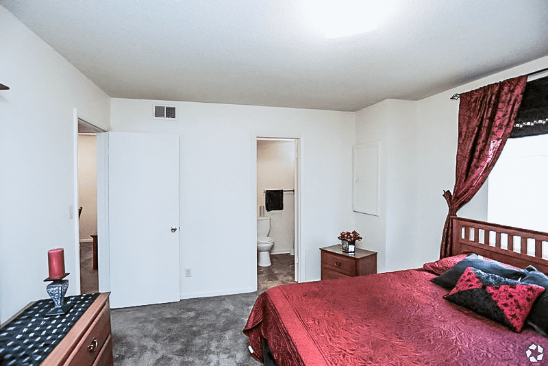 a bedroom with a red bed and a bathroom with a toilet at Gatehouse Apartments, Missouri, 64134
