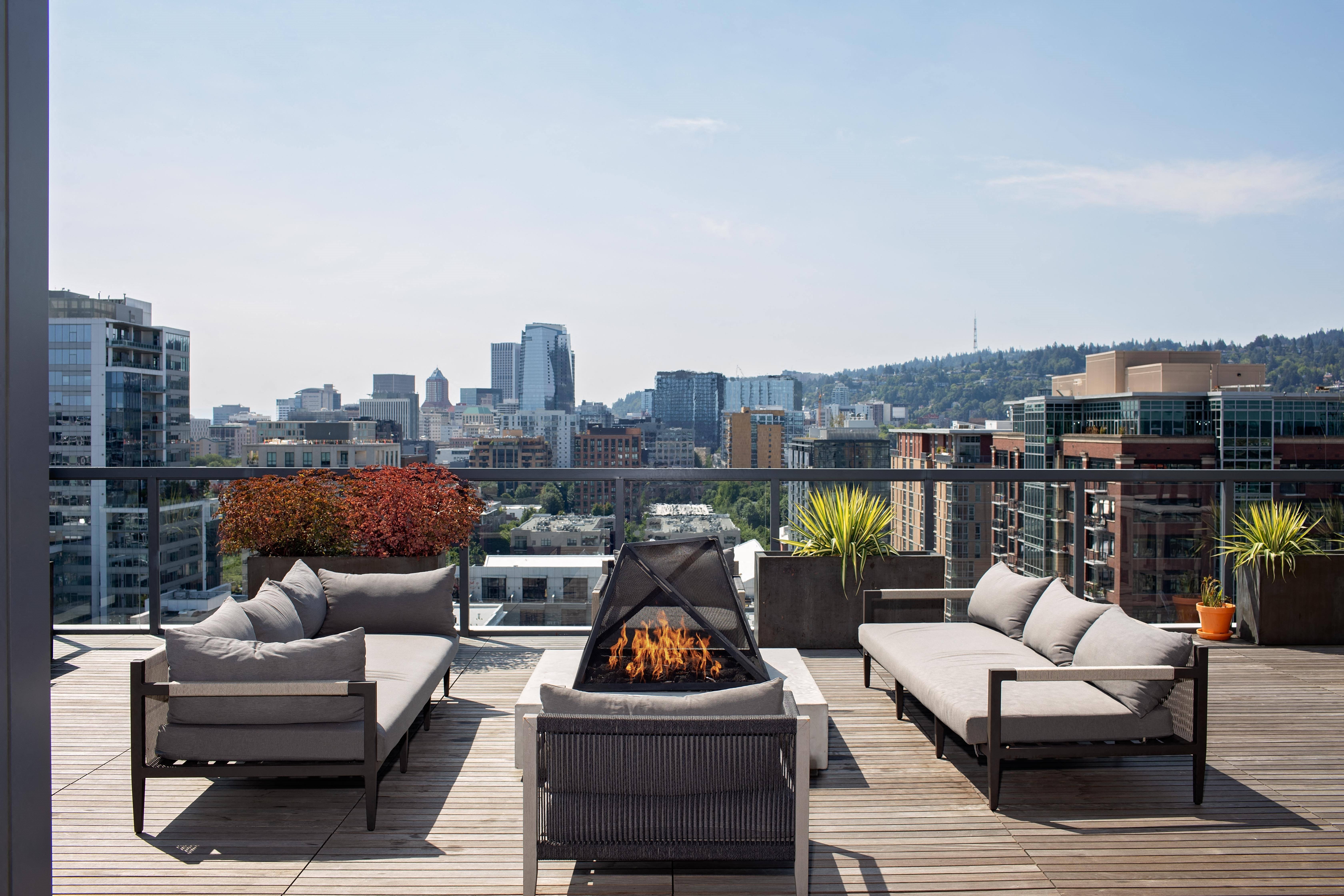 a roof deck with chairs and a fire pit overlooking a city