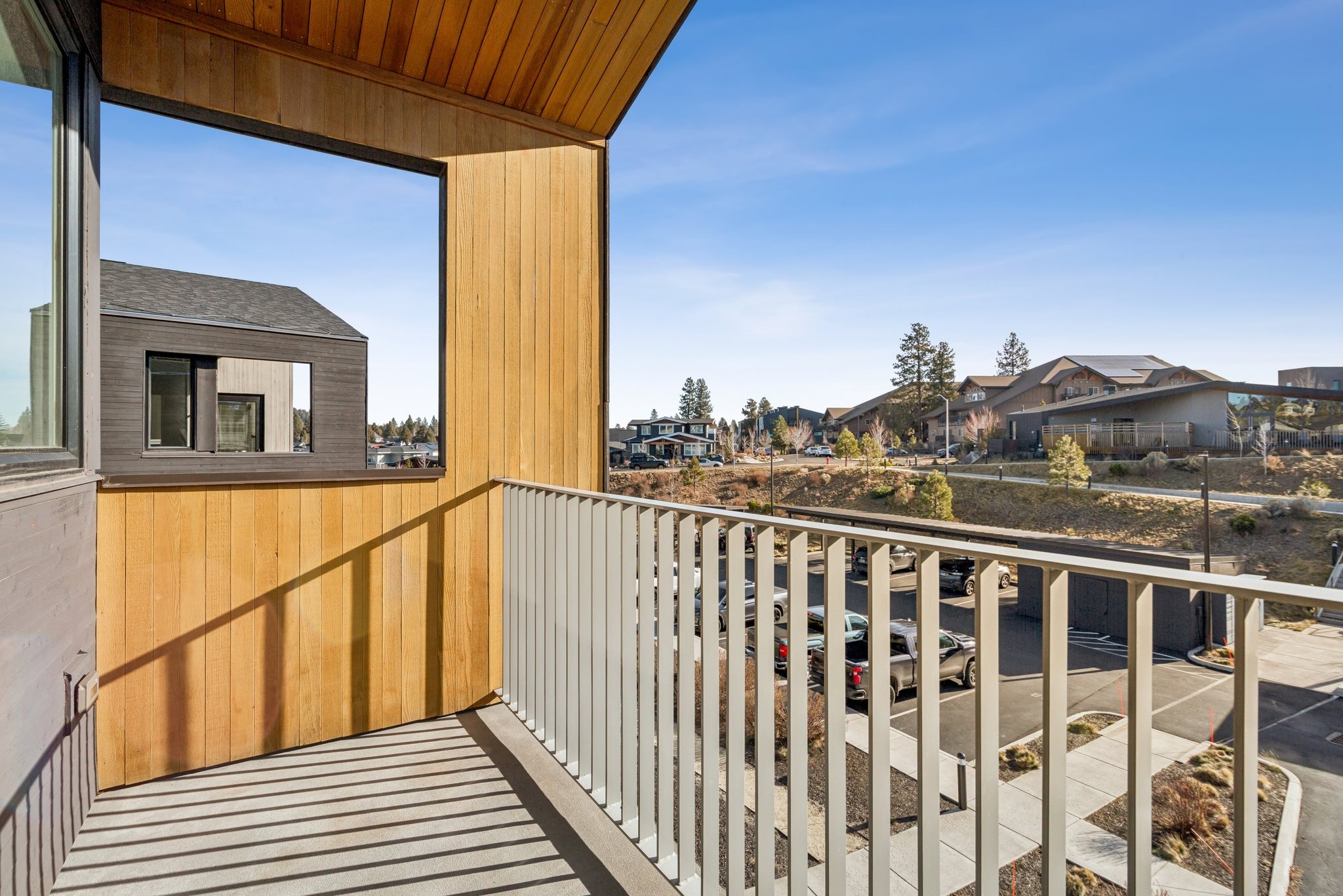 A balcony with a wooden railing and a view of a parking lot and buildings.