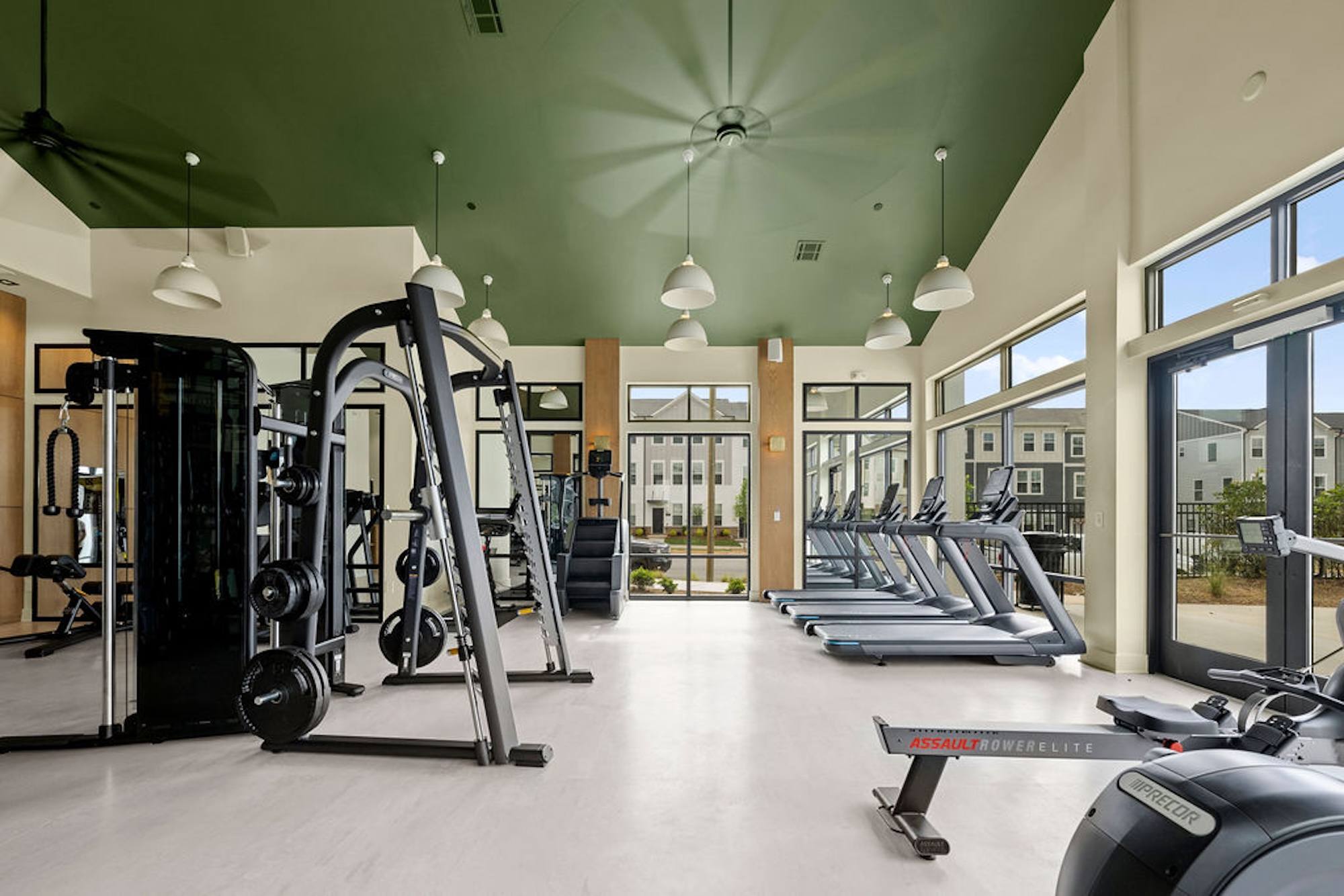 A modern apartment fitness center featuring a functional workout rig, kettlebells, dumbbells, and weight benches.