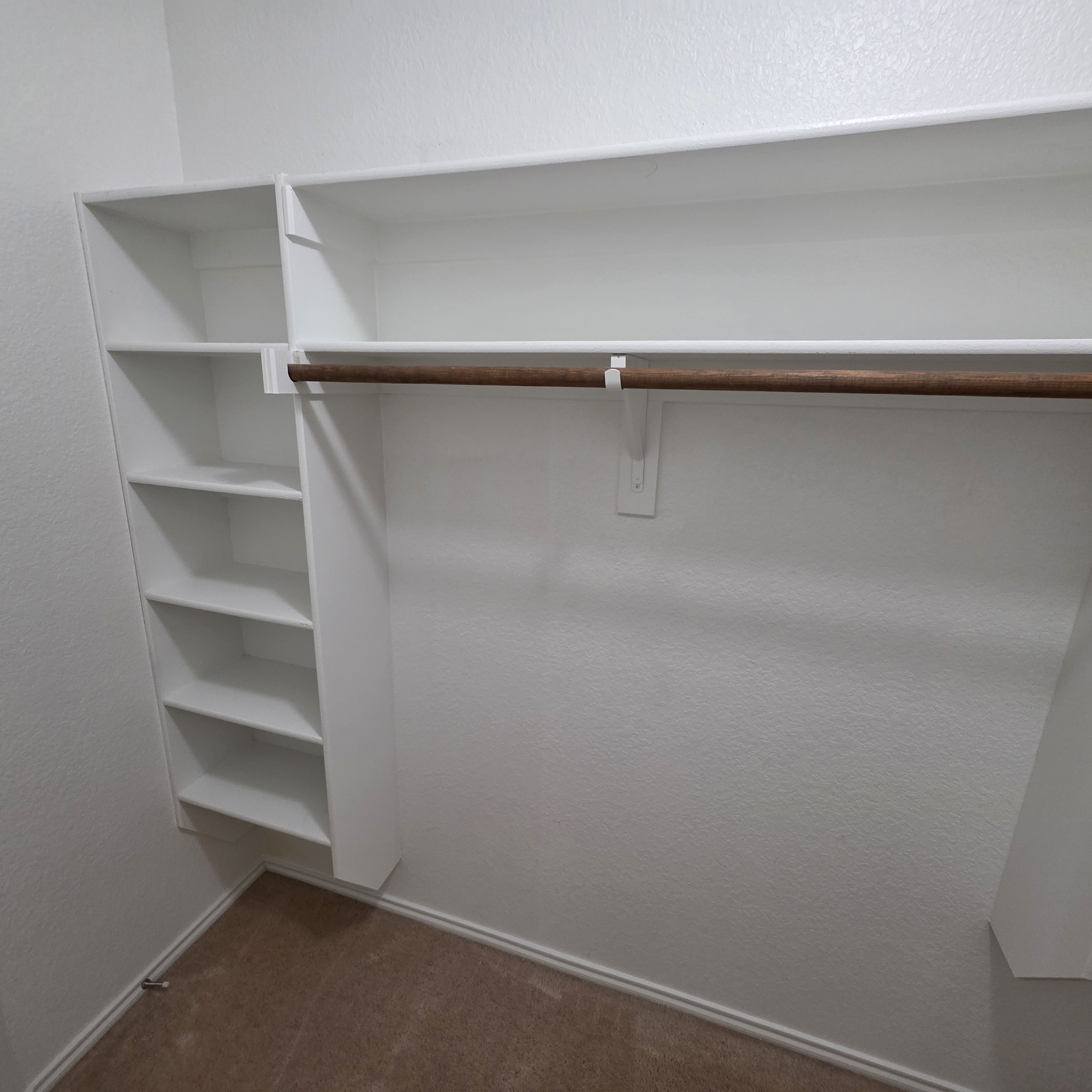 A white shelving unit with a brown bar and a white wall.