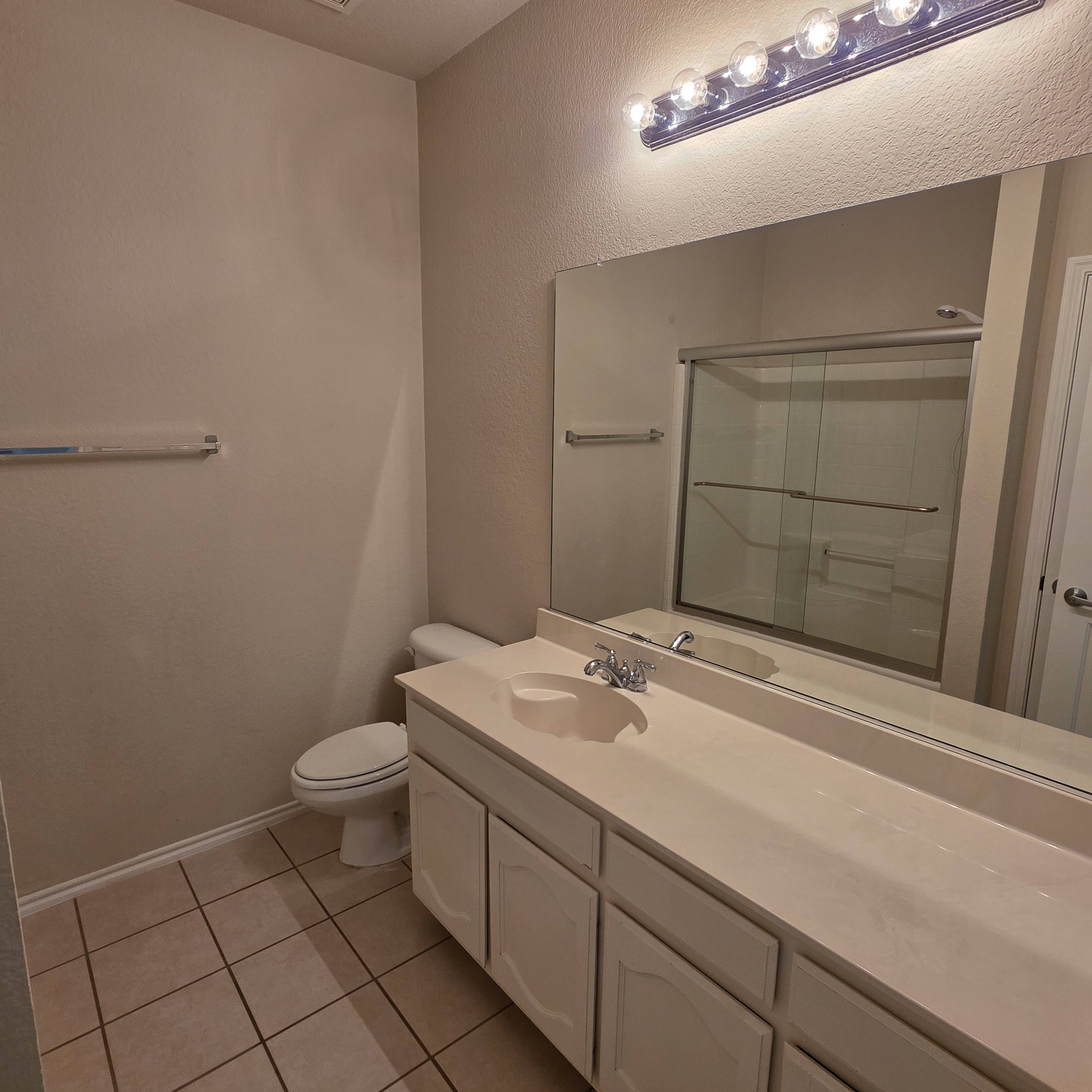 A bathroom with a toilet, sink, mirror, and lights.