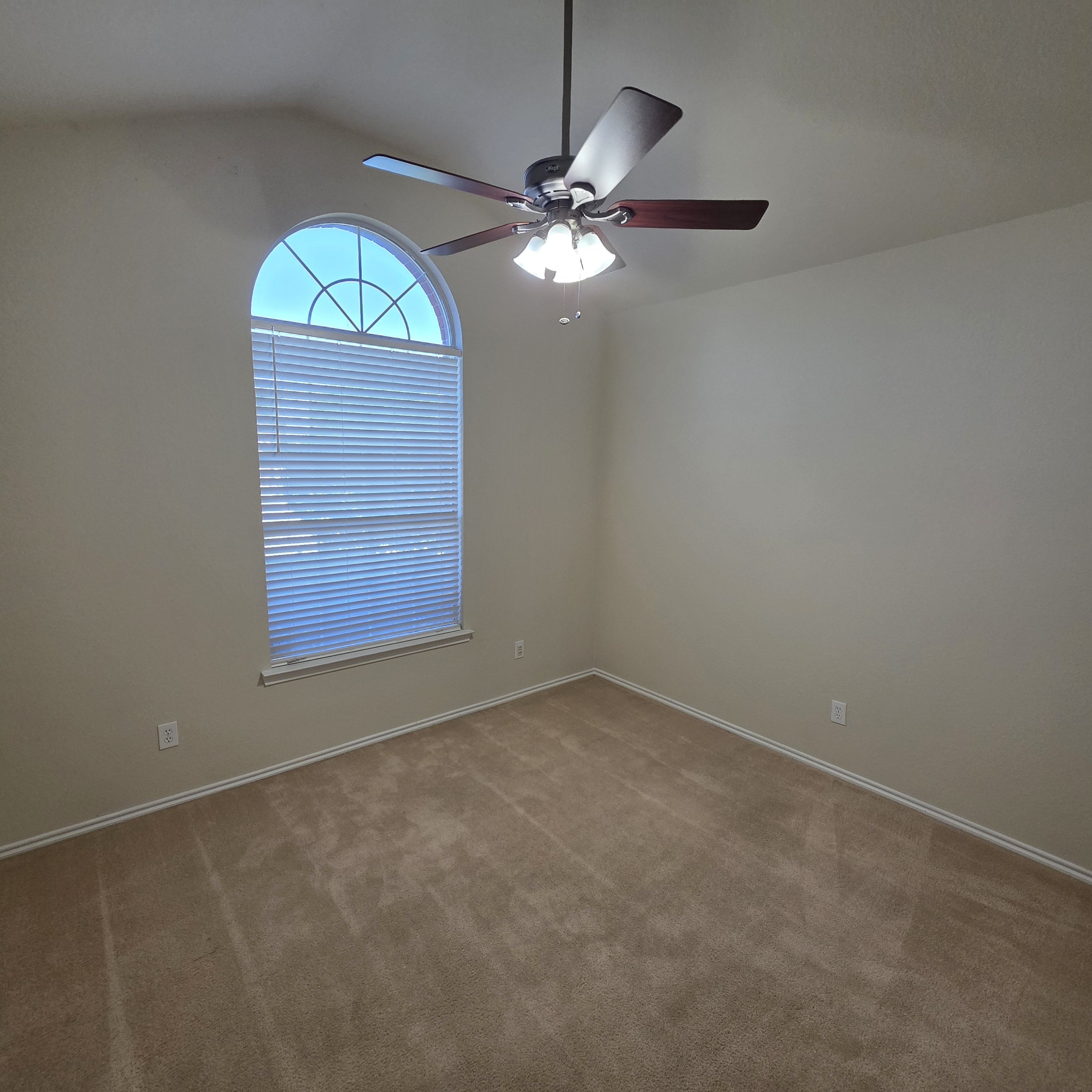 A room with a ceiling fan and a window with blinds.