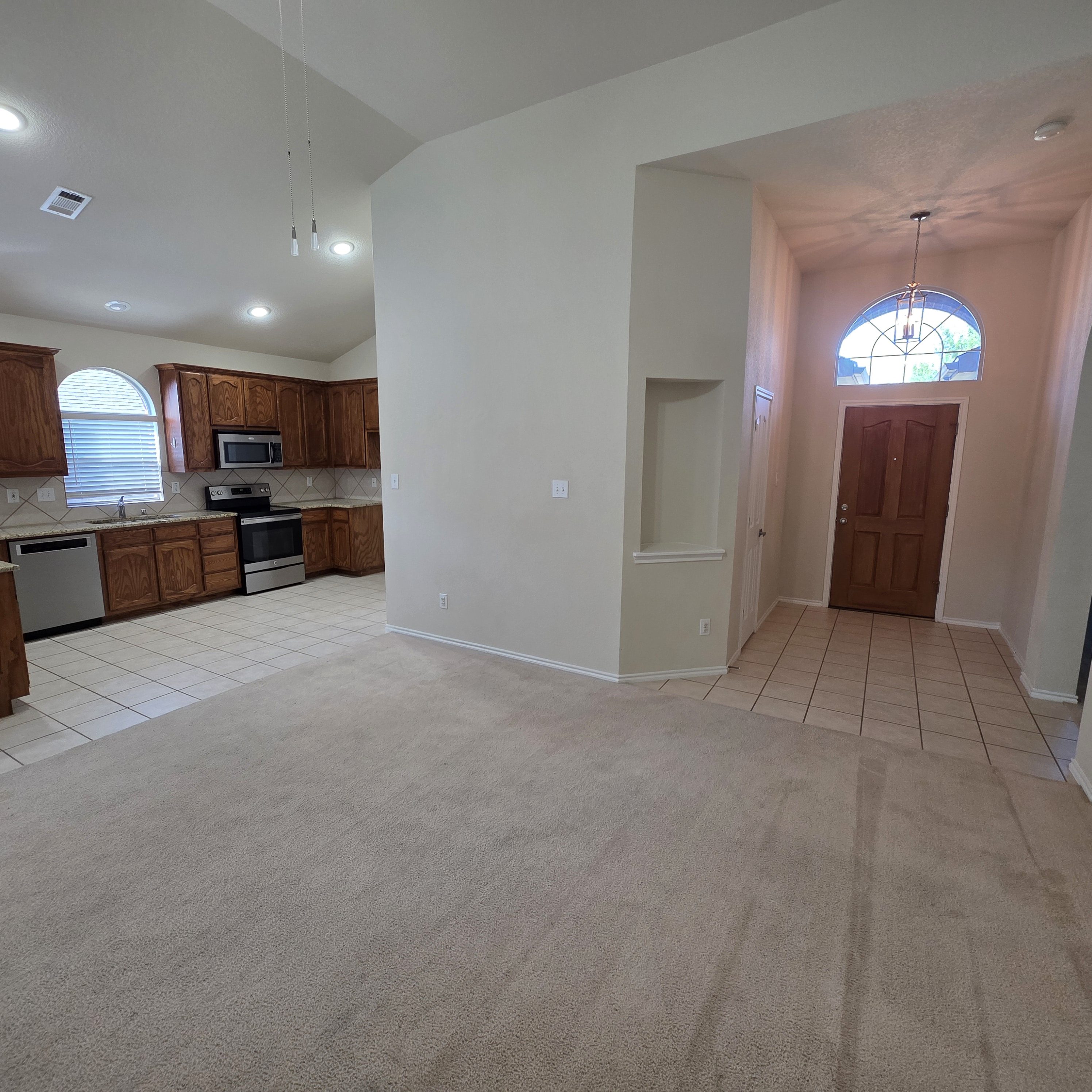 A large, empty room with a kitchen area to the left and a doorway leading to another room to the right.