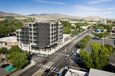 A large grey building is in the middle of a street with cars and a bus.