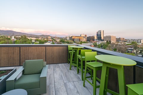 A patio with green chairs and tables overlooking a city skyline.