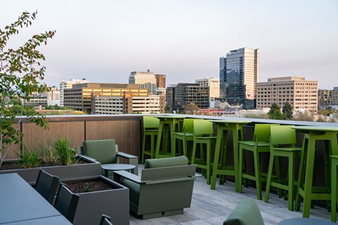A rooftop patio with green chairs and tables overlooking a city skyline.