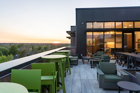A patio with green chairs and tables overlooks a sunset.