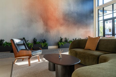 A living room with a chair, a sofa, a table, and a wall mural.
