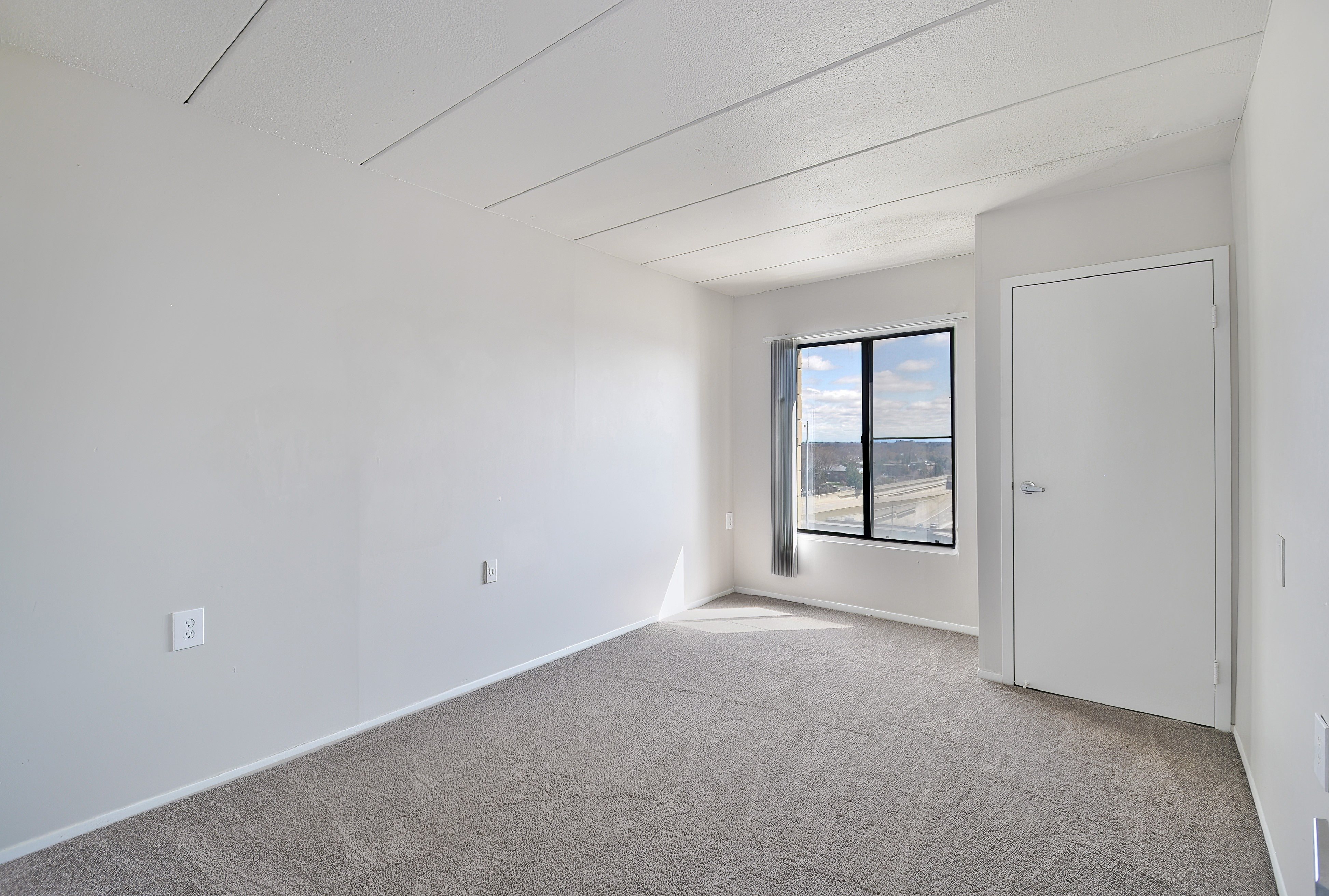 A room with a carpeted floor and a window with a view of the outside.