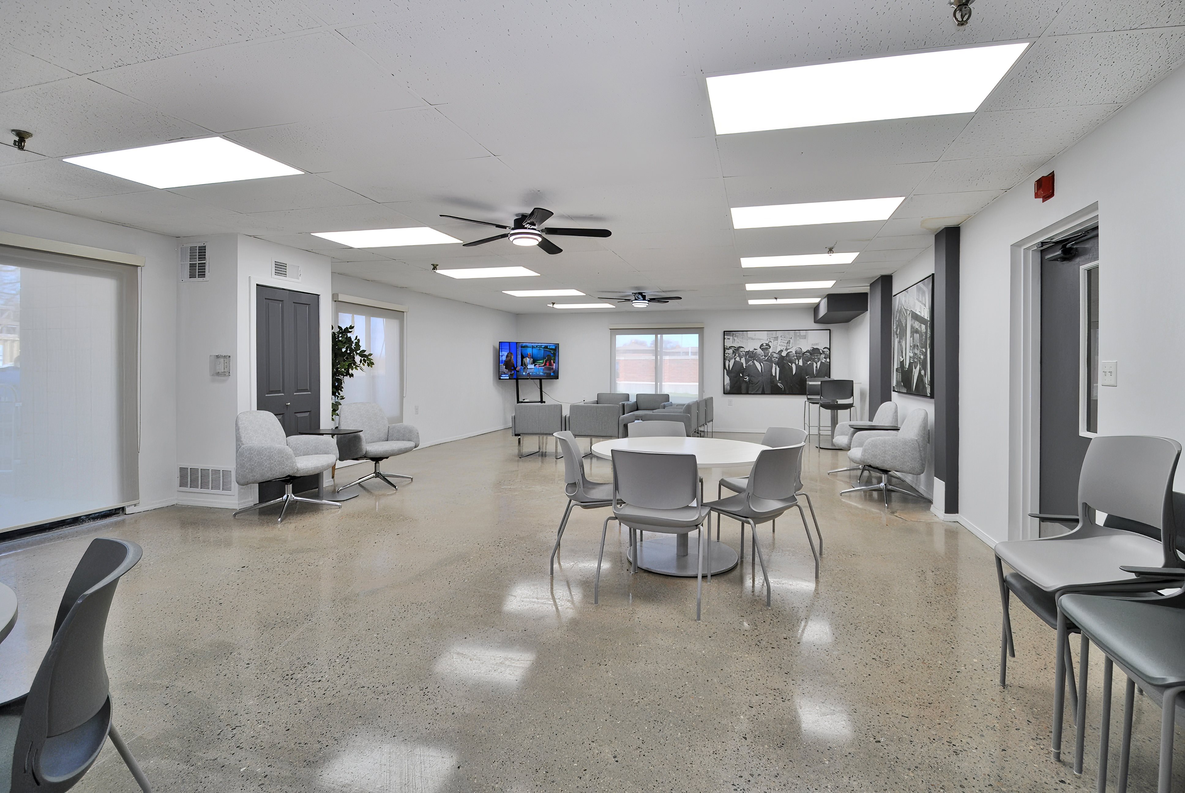 A room with a white ceiling and a grey floor with chairs and tables.