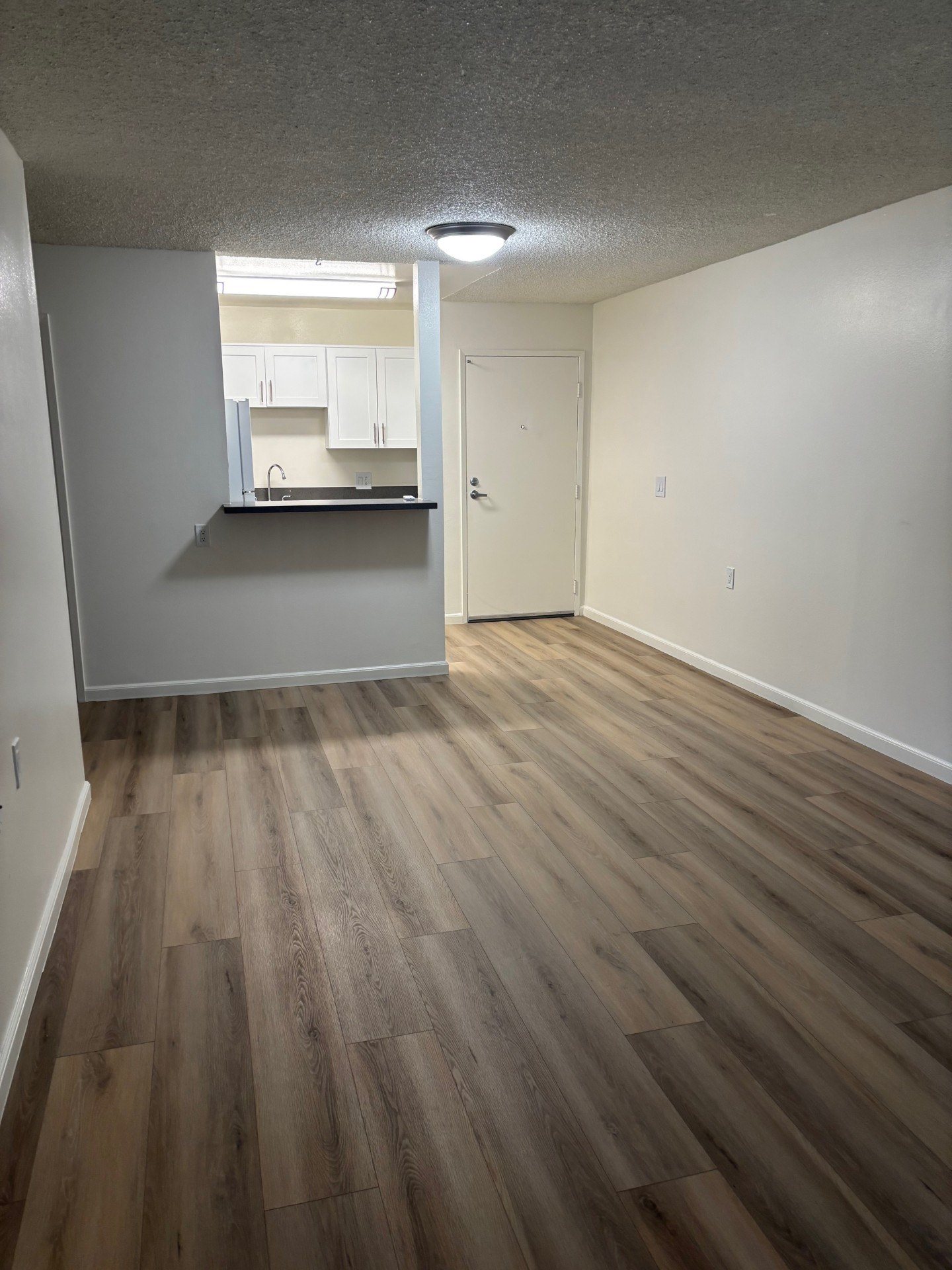 A room with wooden flooring and a kitchen in the background.