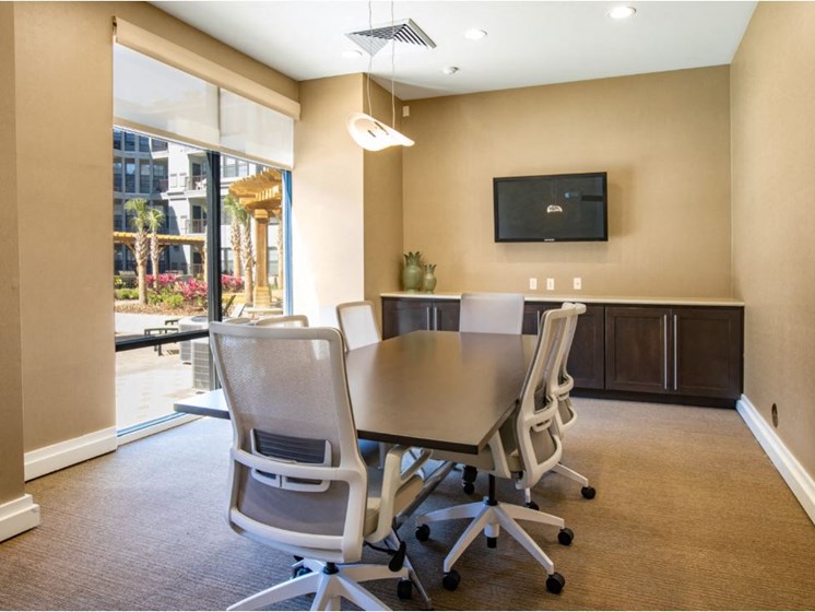 Business center with conference table with chairs and TV & printer.