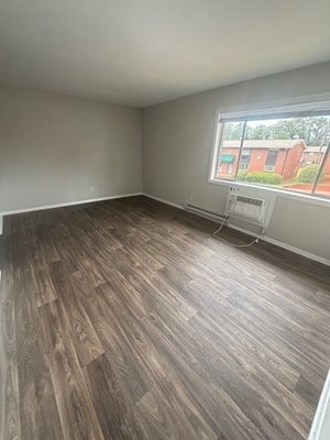 A room with wooden flooring and a window overlooking a red building.