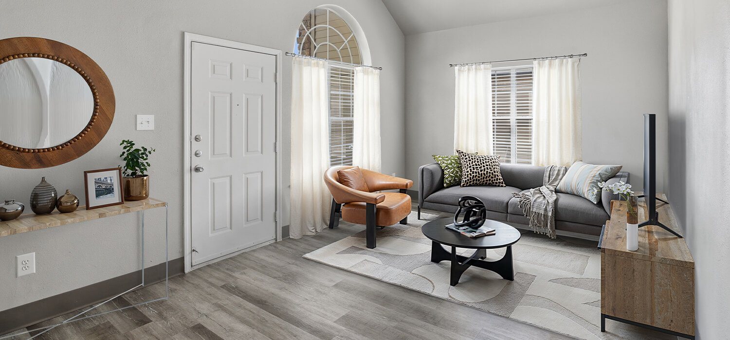 A living room with a grey sofa, a round mirror, a coffee table, and a TV.