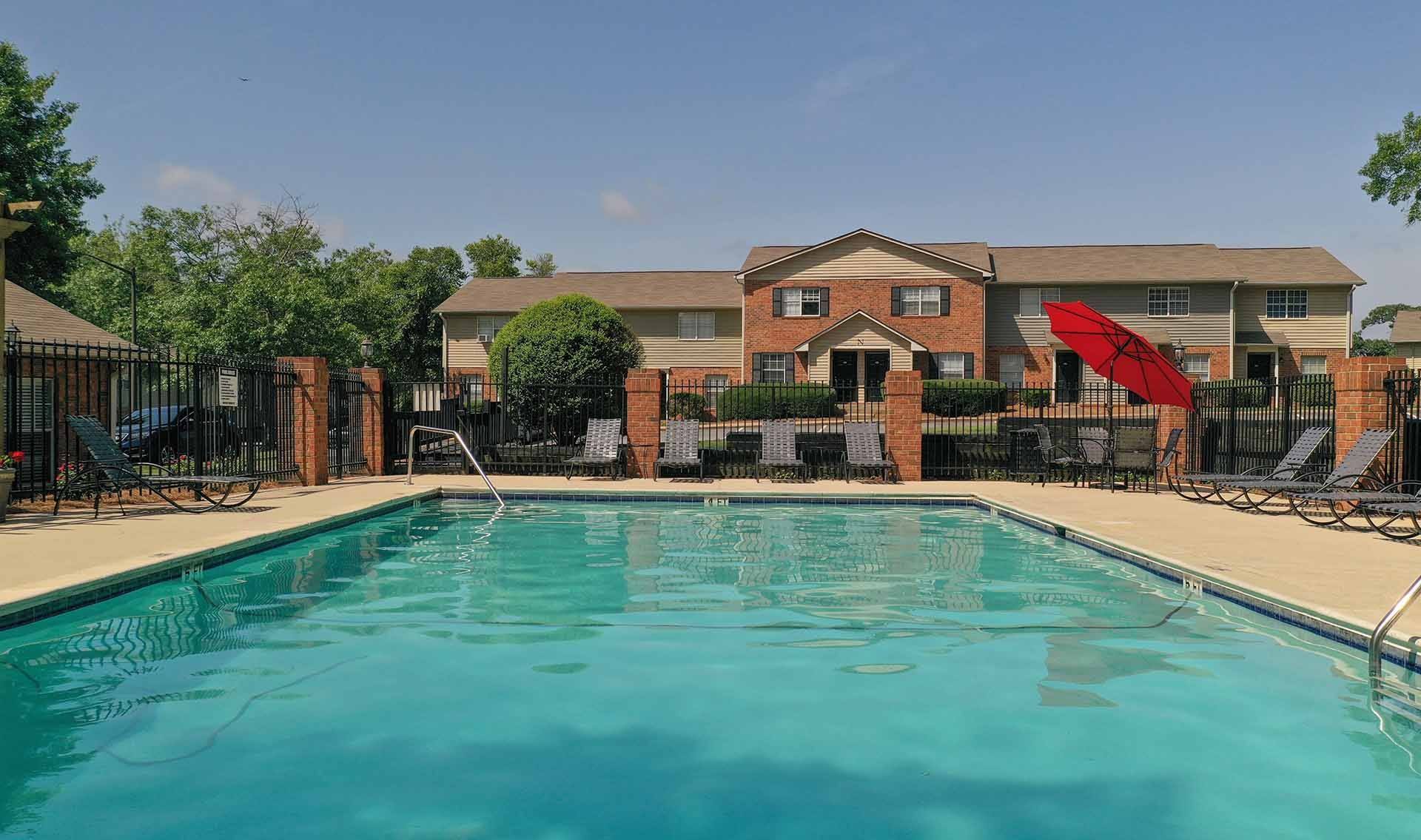 A swimming pool in front of a brick building with a red umbrella.