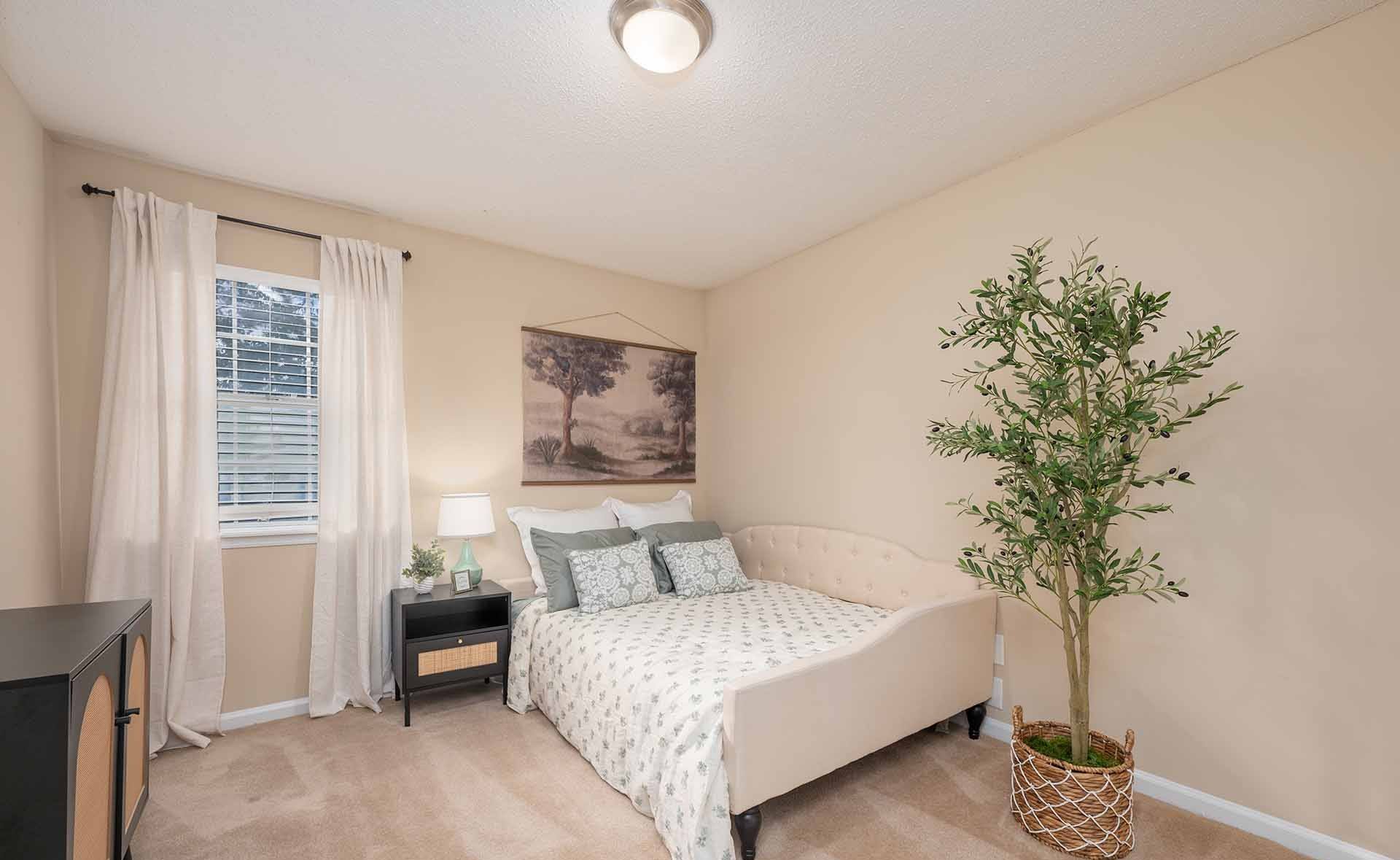 A bedroom with a bed, nightstand, and a plant.