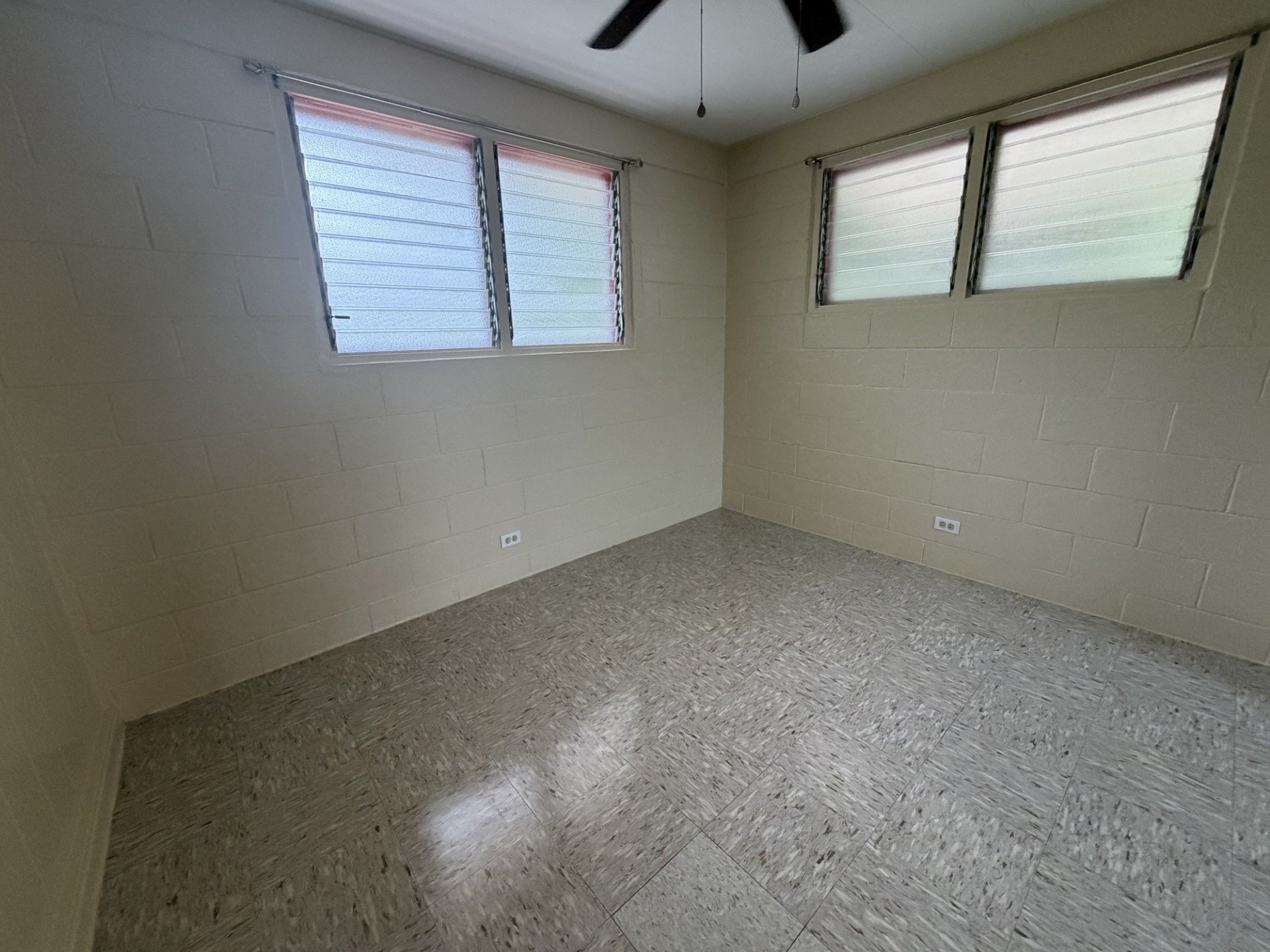 A room with a ceiling fan and two windows.