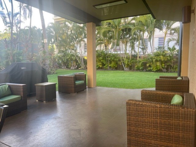 A patio with wicker furniture and a view of a lush green lawn.