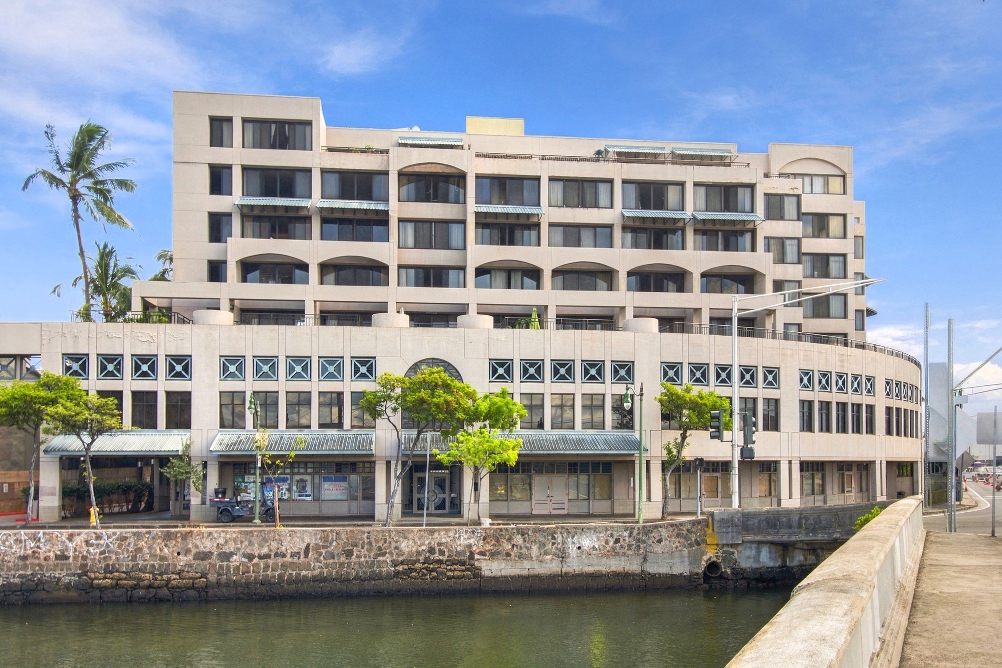 A large white building with a green awning sits next to a body of water.