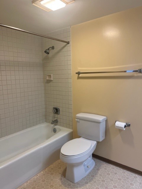 A white toilet is in a bathroom with a white bathtub and a towel bar.