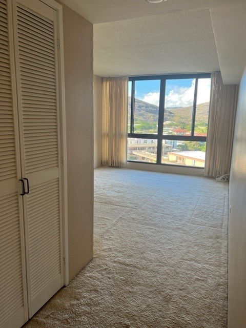 A room with a carpeted floor and a sliding door leading to a balcony with a view of the mountains.