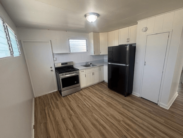 A kitchen with a black fridge and wooden floors.