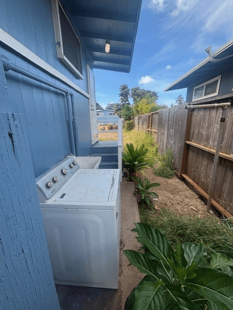 A white washing machine is on the back porch of a blue house.