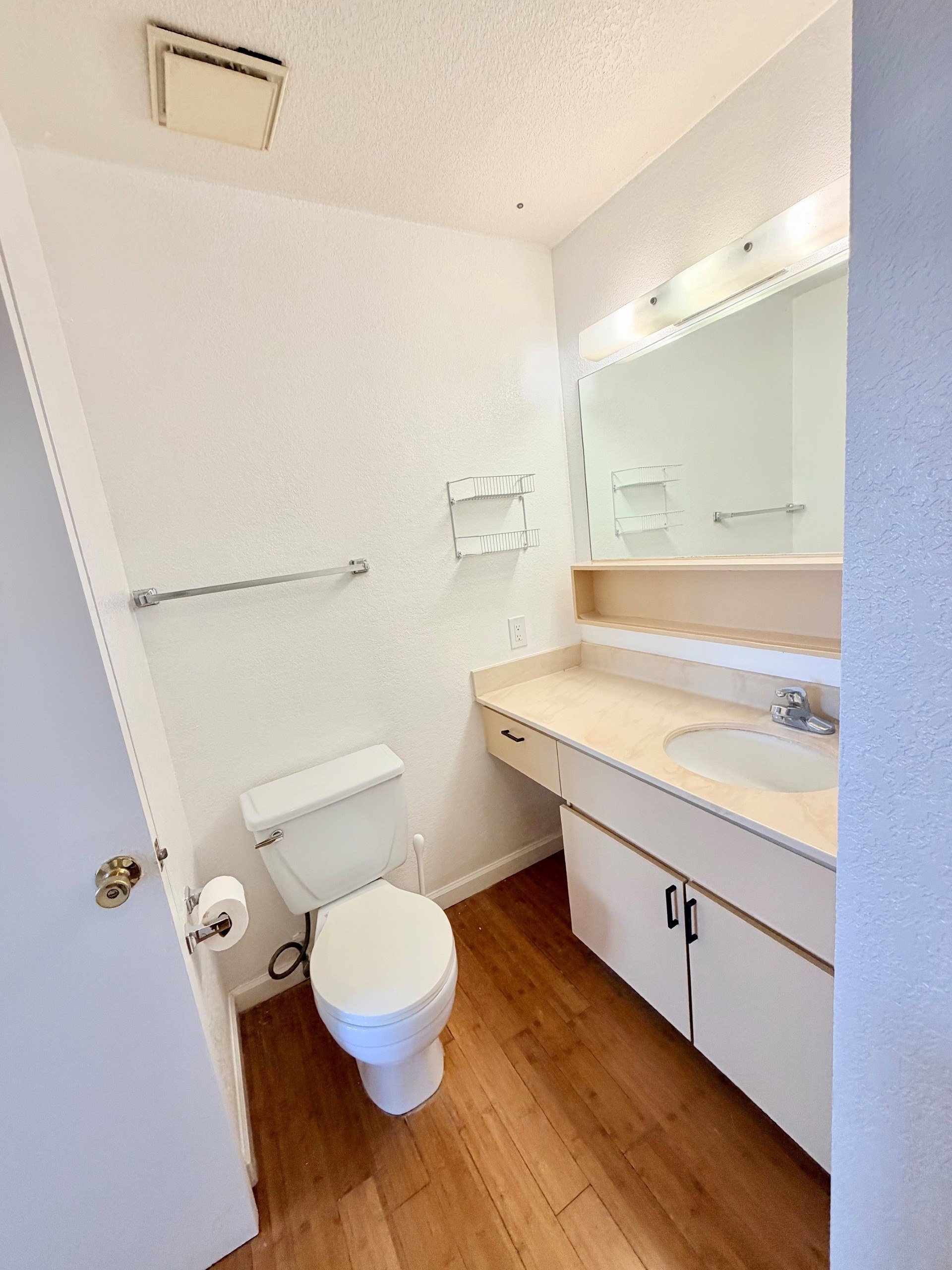 A white toilet is in a small bathroom with a white sink and a white door.