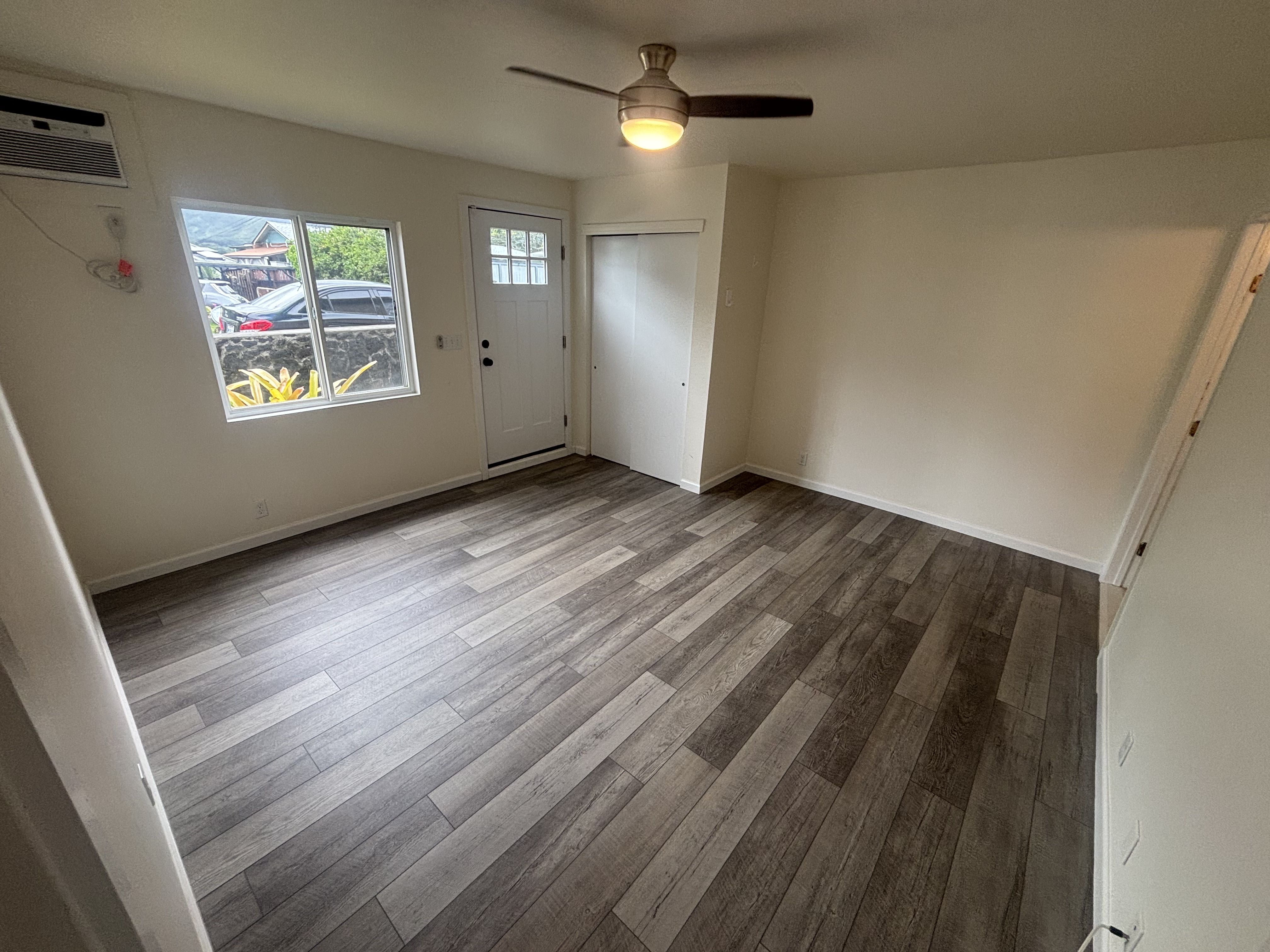 A room with a ceiling fan and a window with a view of a parking lot.