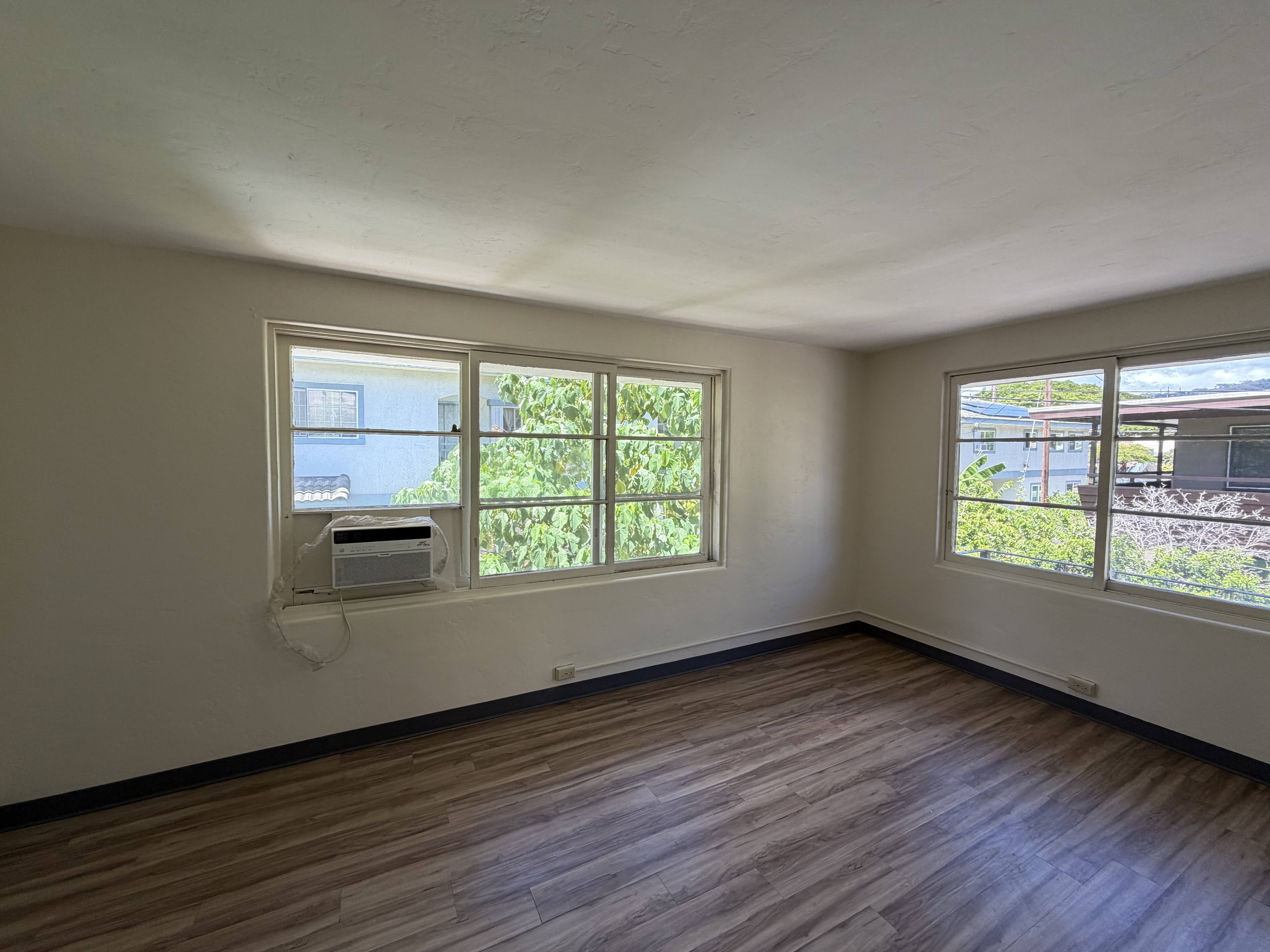 A room with wooden floors and windows overlooking a parking lot.