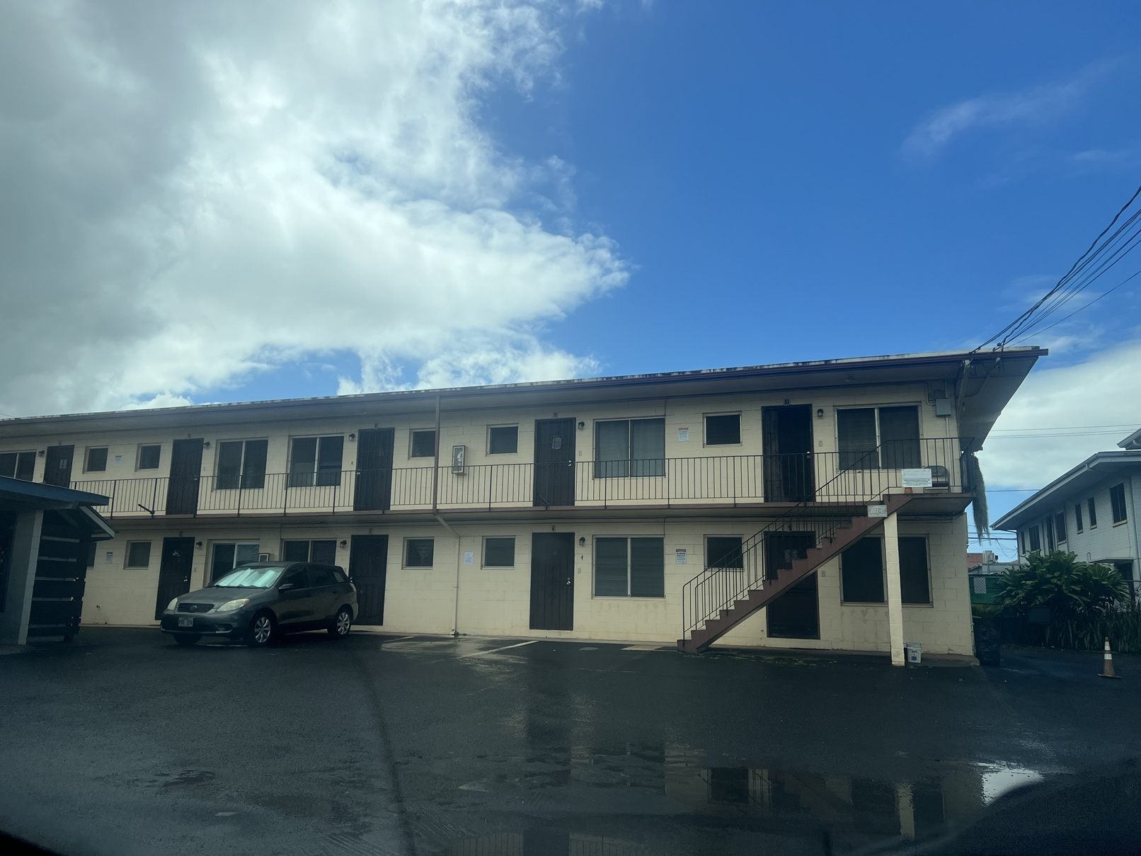 A car is parked in front of a building with a blue sky and clouds in the background.