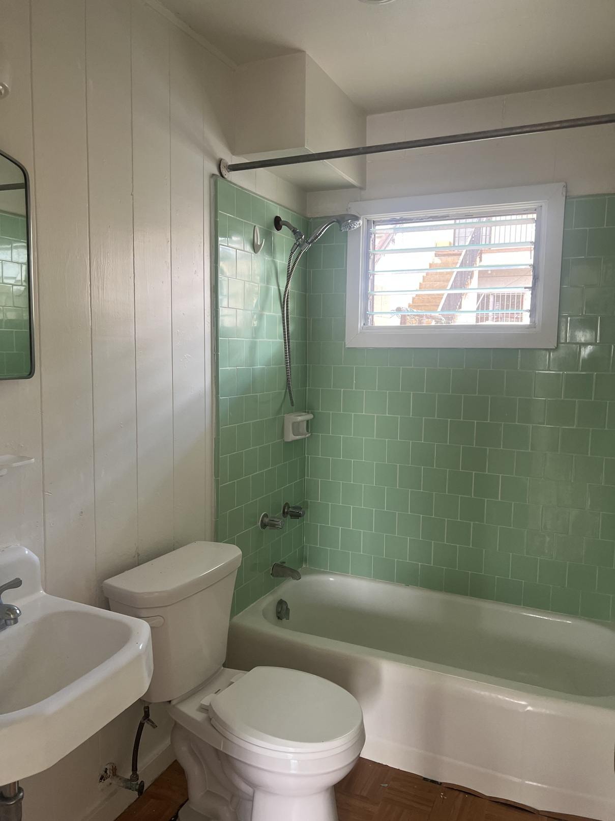 A white toilet sits next to a white sink in a bathroom with green tiles.