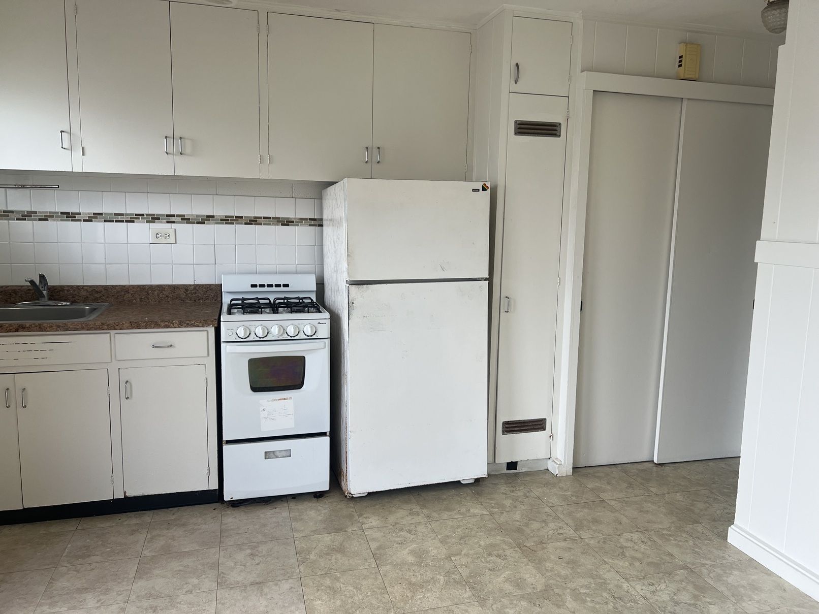 A white refrigerator is in a kitchen with white cabinets.