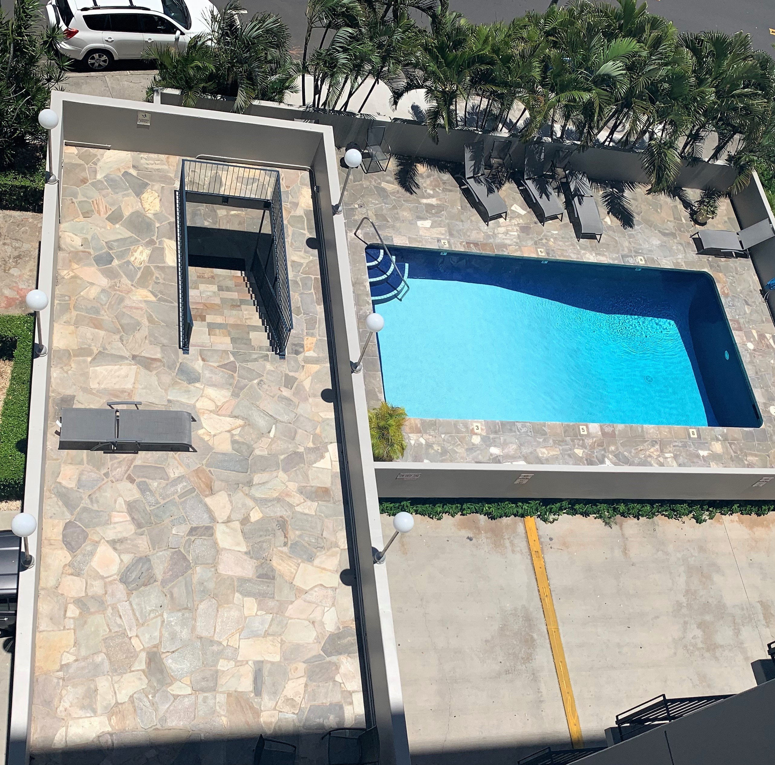A pool with a slide and a stone patio.