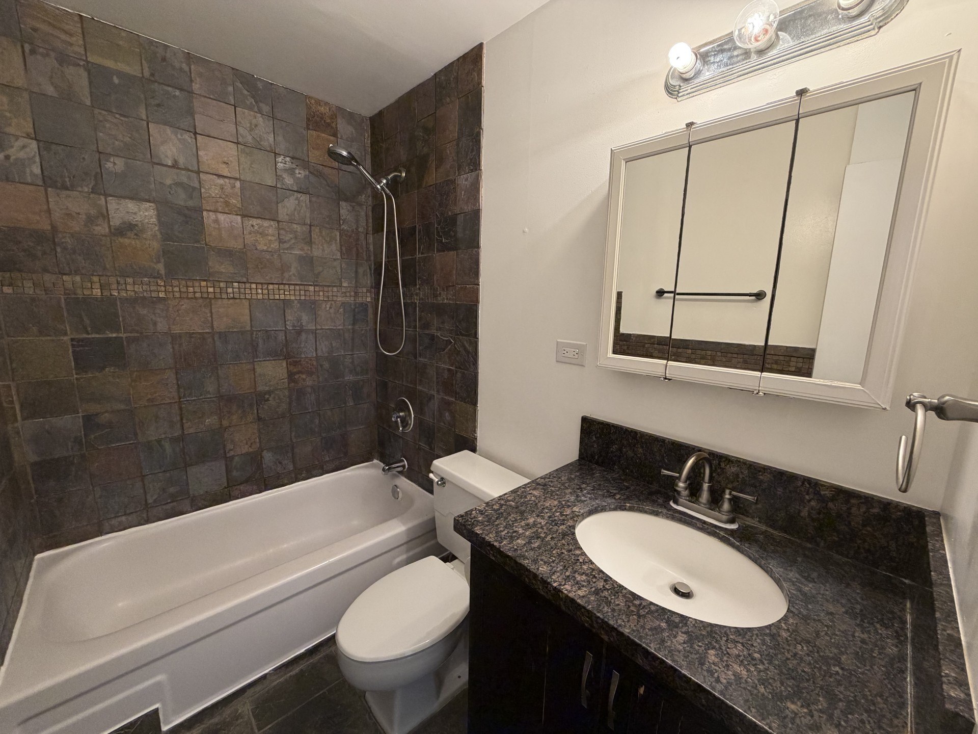 A bathroom with a tiled shower, a white toilet, a sink and a bathtub.