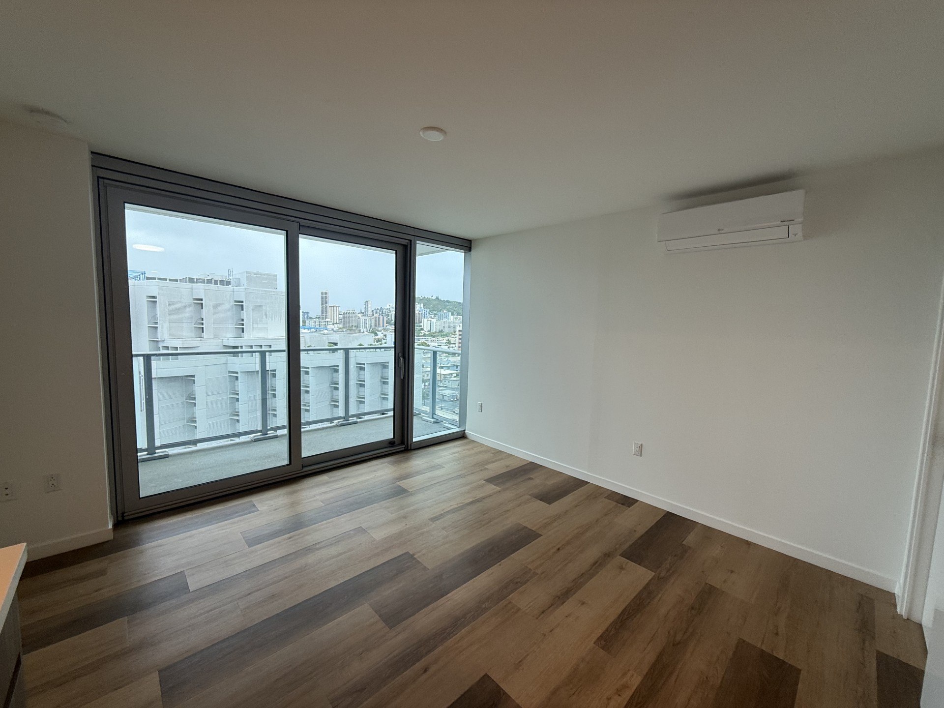 A room with wooden flooring and a large window overlooking a cityscape.